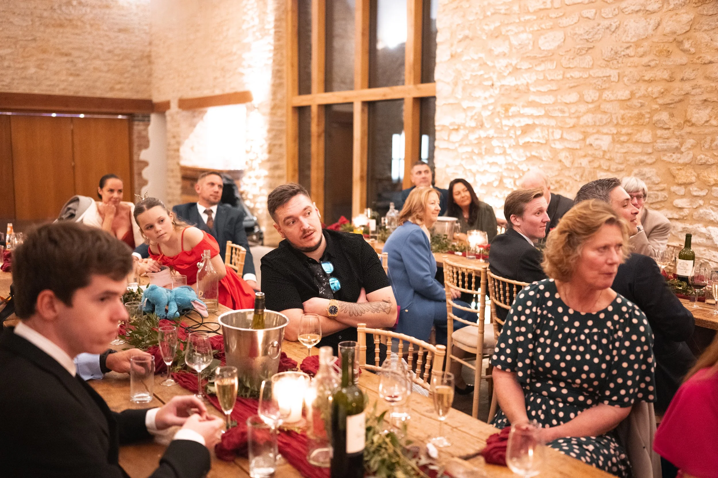 People seated at a decorated dinner table during a celebration or gathering in a warmly lit room with rustic stone walls and wooden accents.