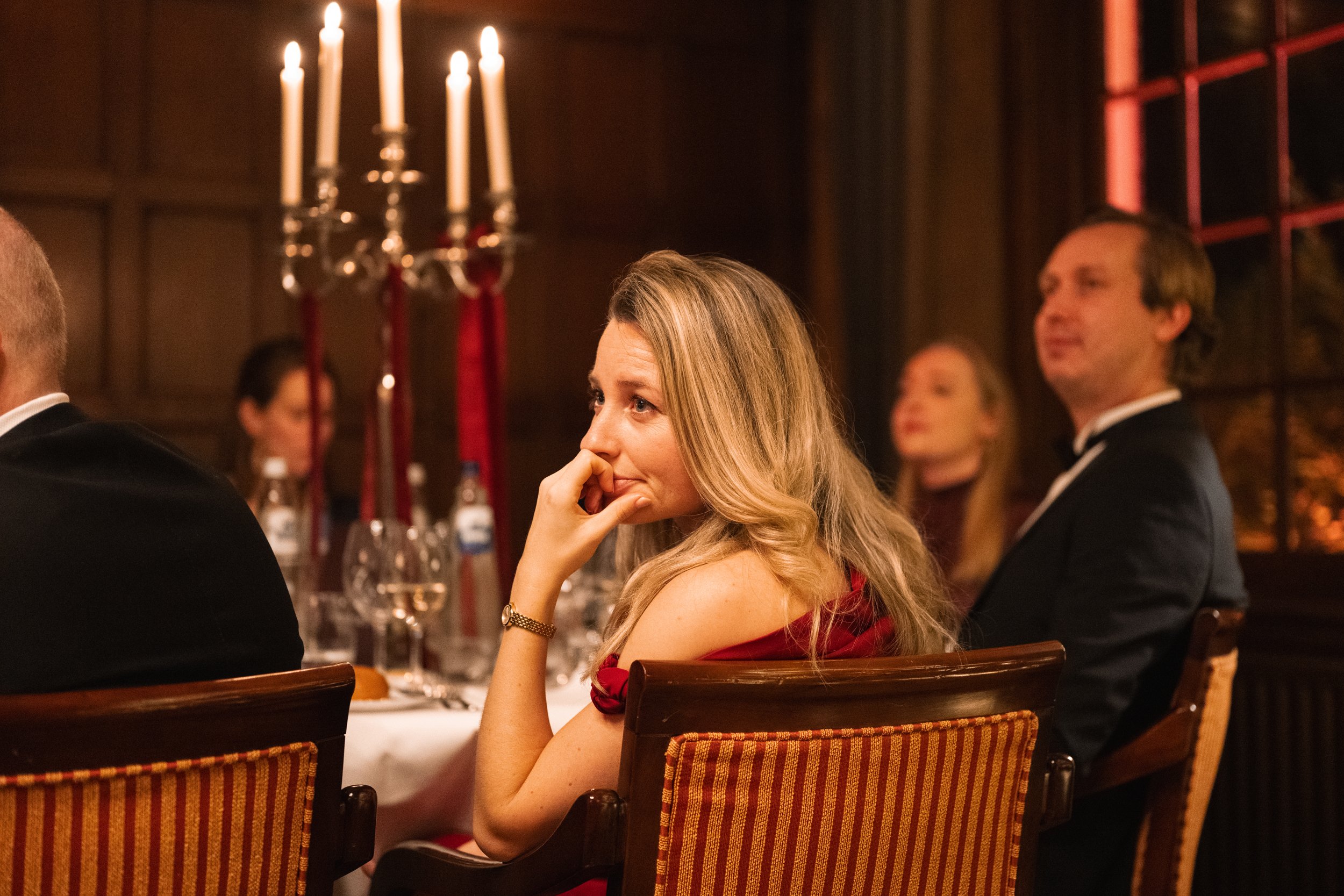 People sitting at a dinner table with lit candelabra, engaging in a formal event or gathering.