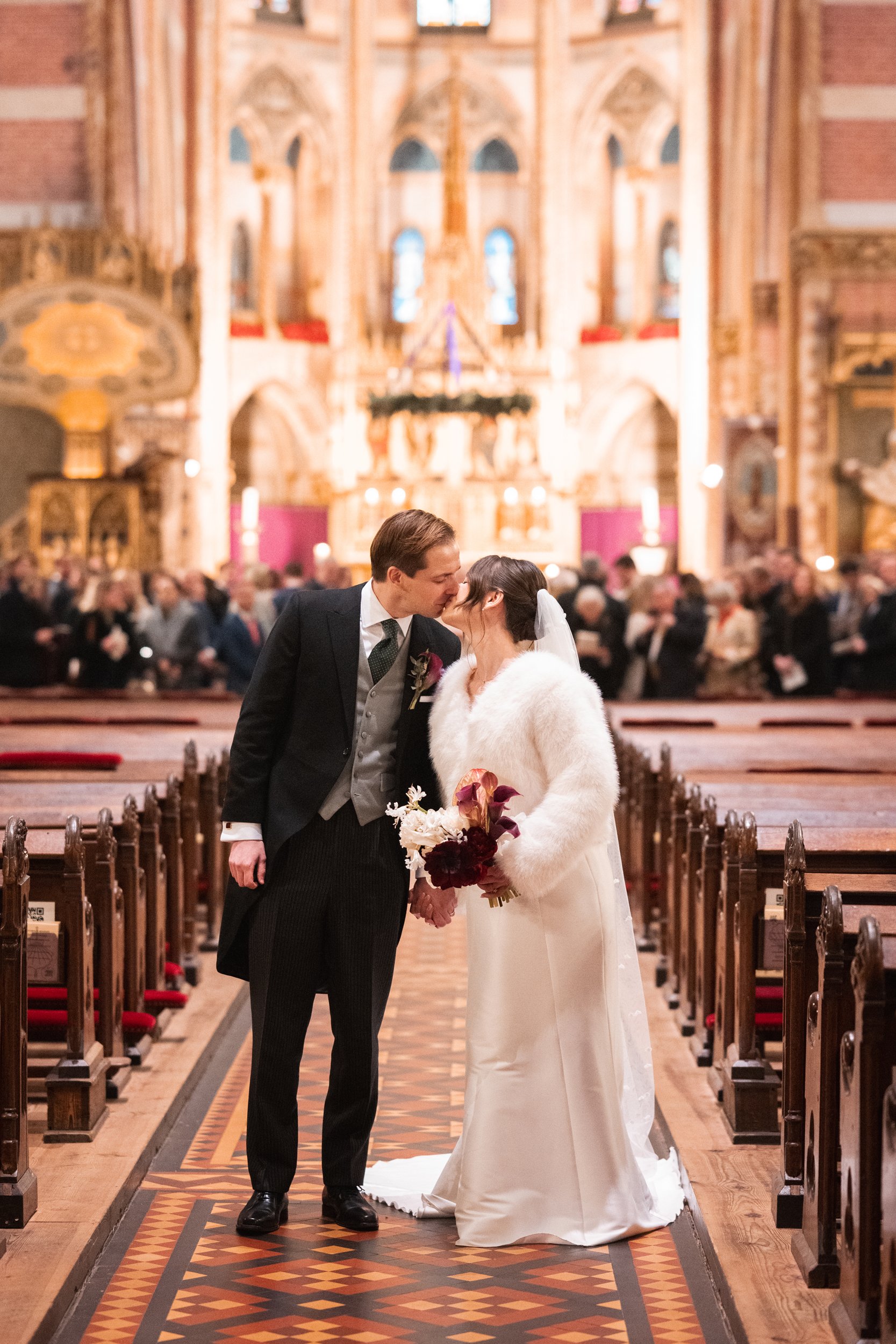 A bride and groom share a kiss in a church after their wedding, with guests in the background.