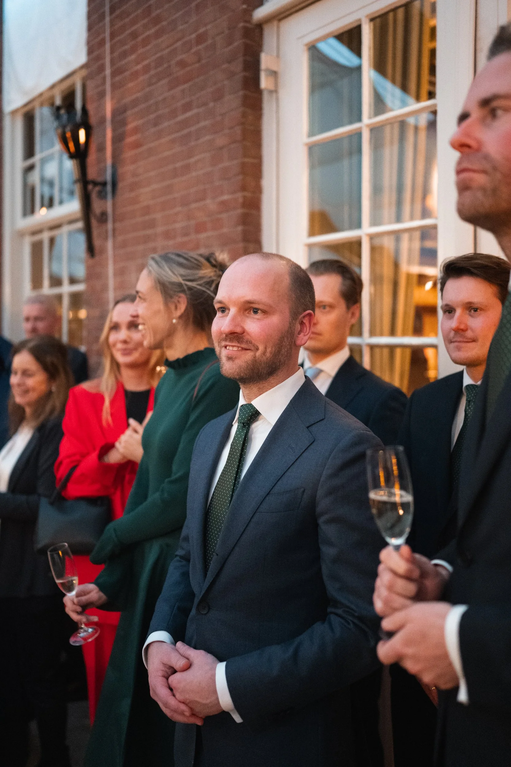 A group of people dressed in formal attire standing together at an indoor event, some holding glasses of champagne.