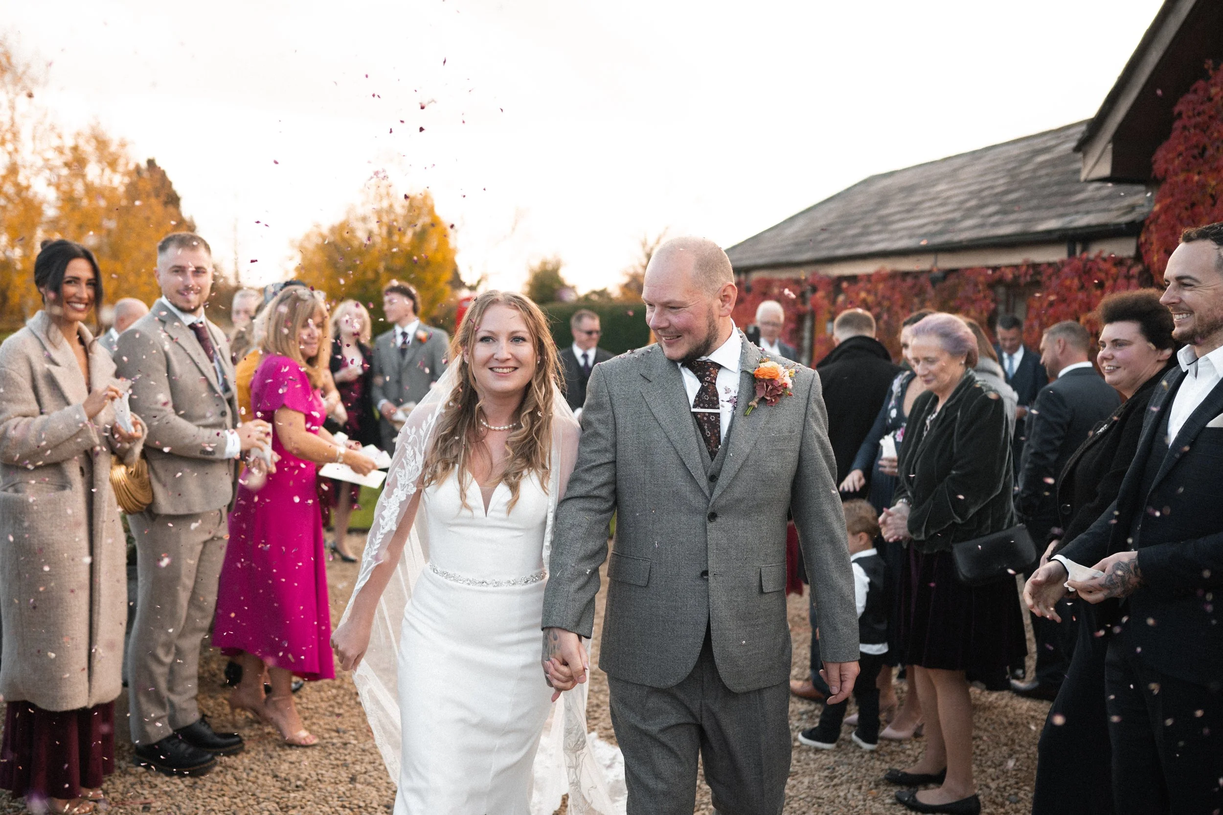 A bride and groom walking hand in hand through a crowd of wedding guests outside during daytime, celebrating their wedding.