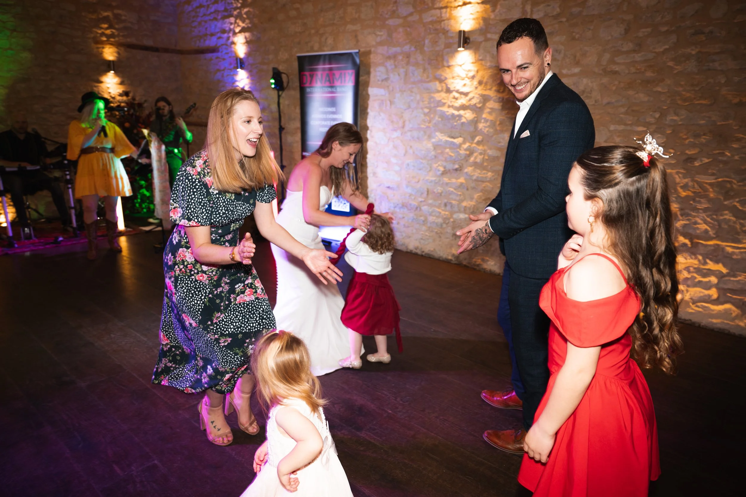 People dancing and enjoying at a party or celebration in a warmly lit venue with a band performing in the background.