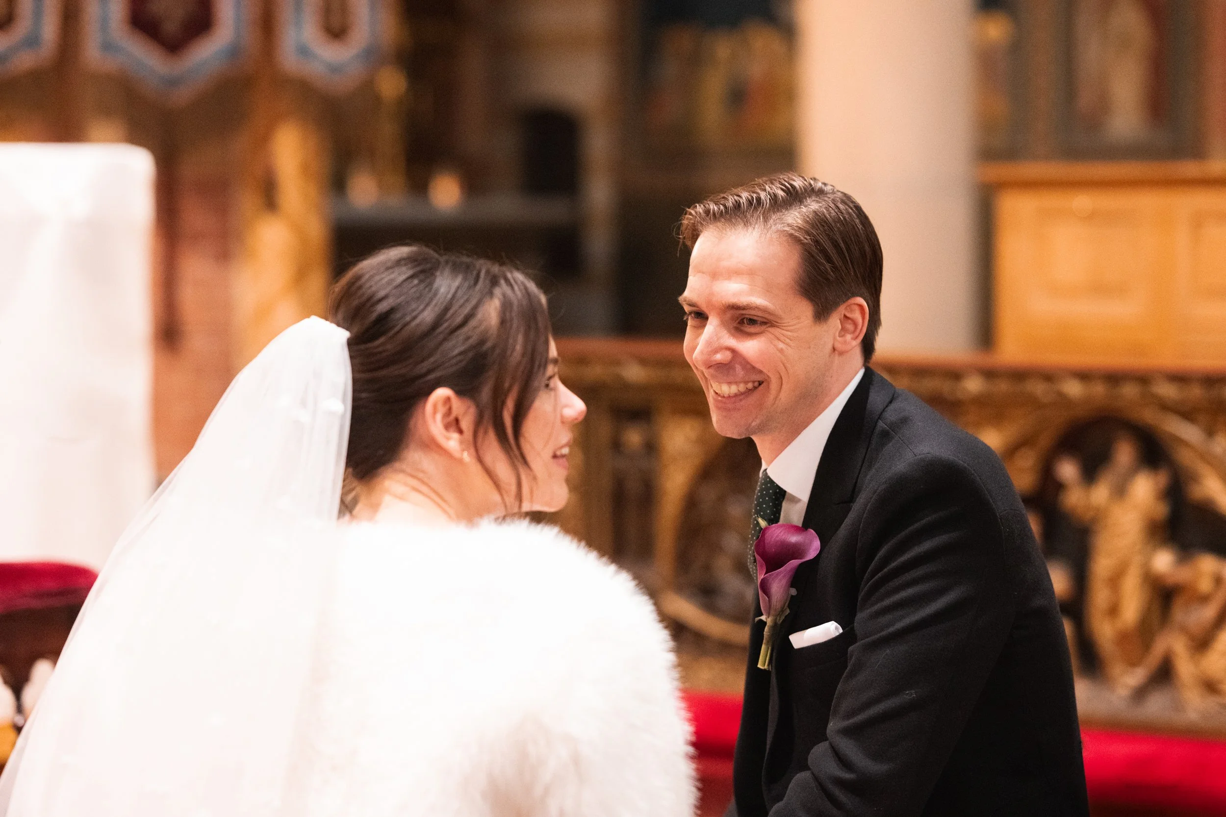 A bride and groom smiling at each other during their wedding ceremony in a church or castle setting.