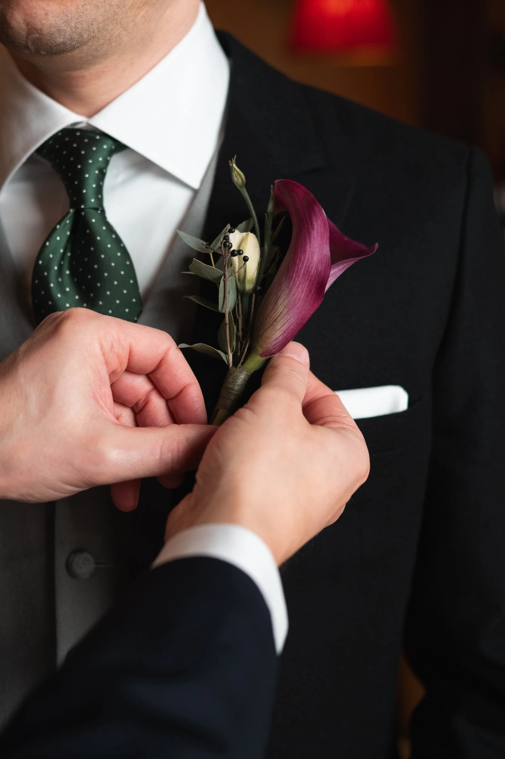 Person pinning a boutonniere to a man's suit jacket during a formal event.