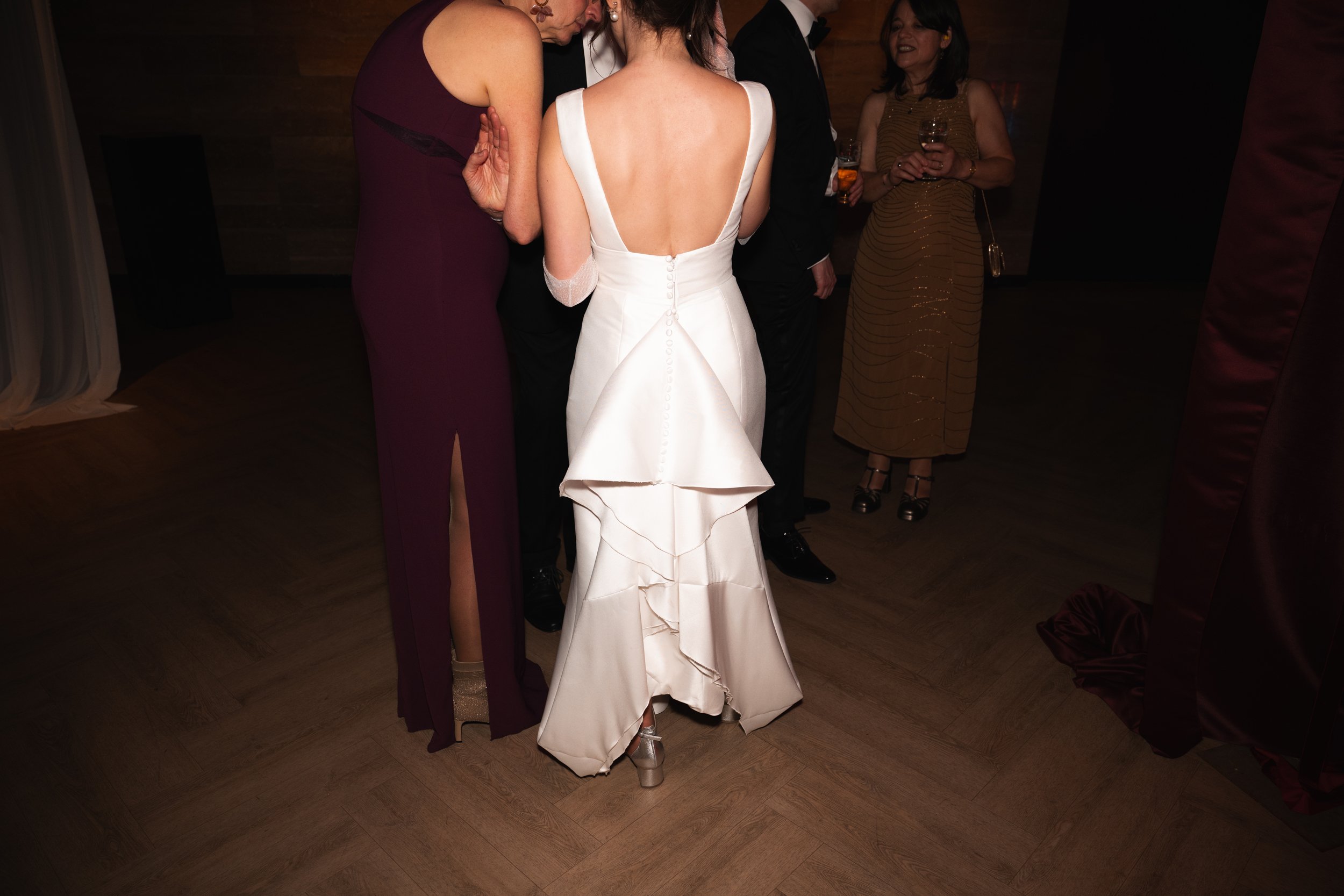A group of people in formal attire gathered closely together at an indoor event, with a woman in a white gown in the center.