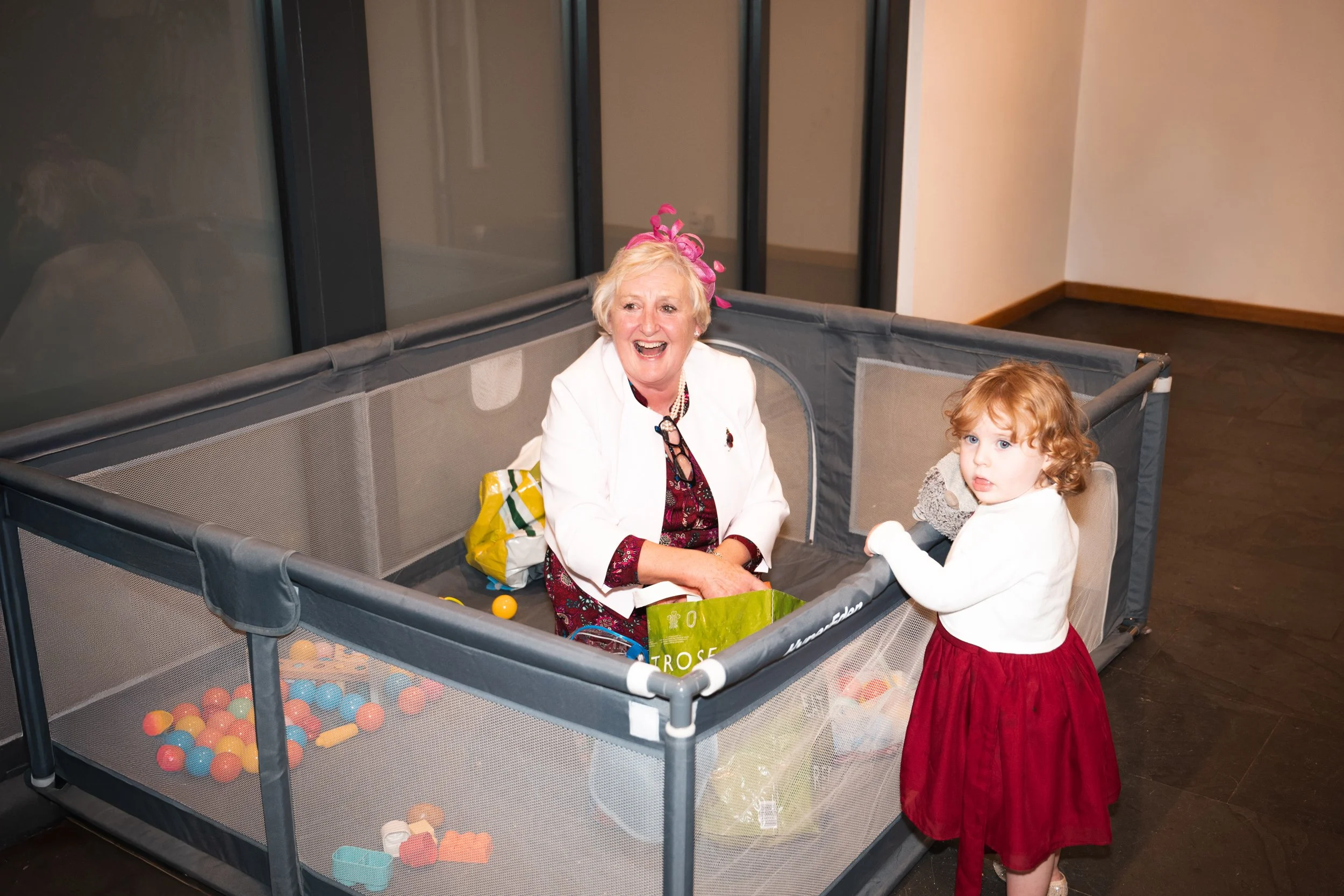 An elderly woman and a young girl standing next to a ball pit with toys inside.