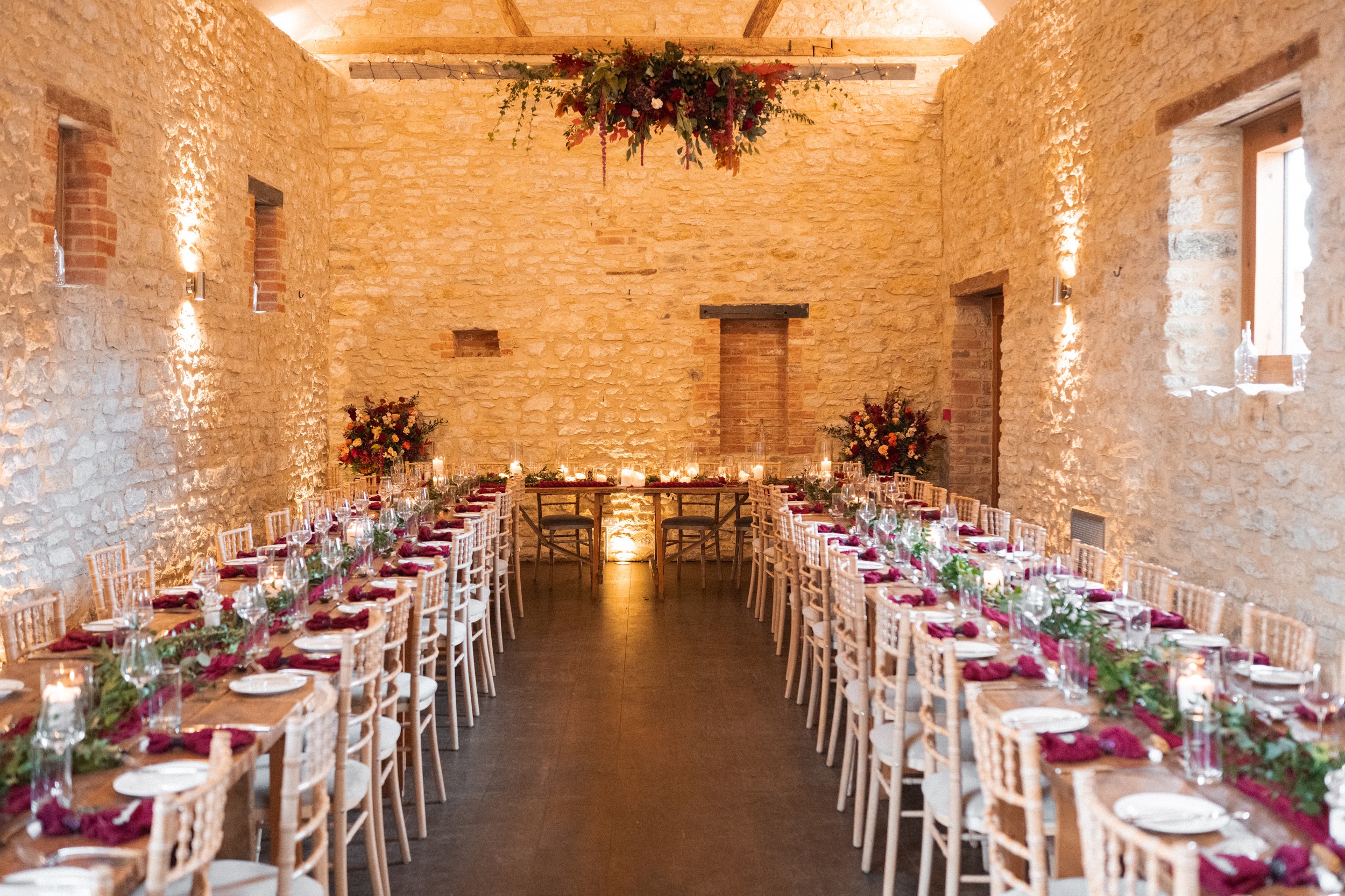 Long dining table set for a wedding reception in a rustic stone-walled room with floral arrangements and candles for decoration.
