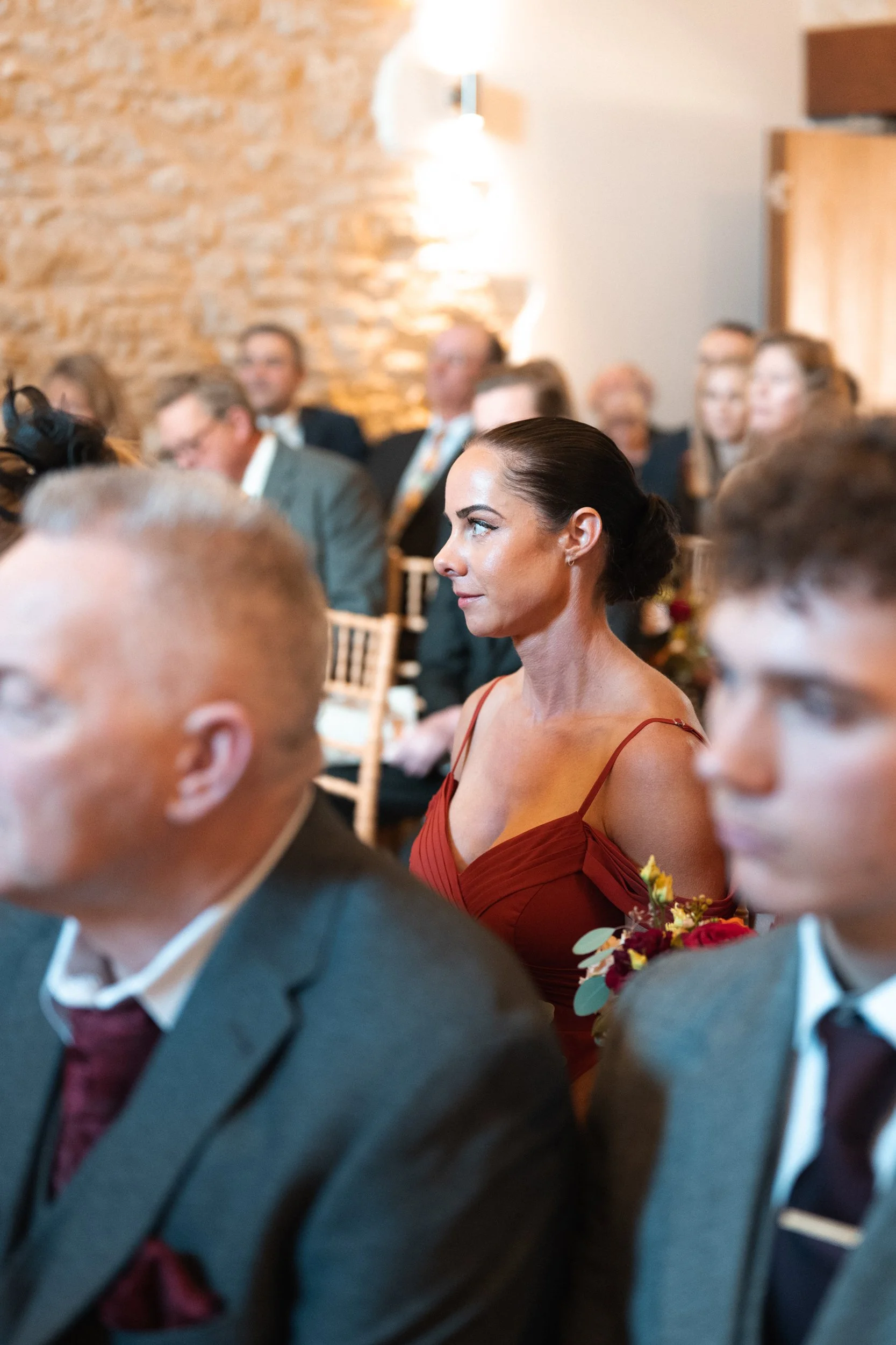A woman in an elegant red dress with spaghetti straps sitting in a formal event, surrounded by other guests.