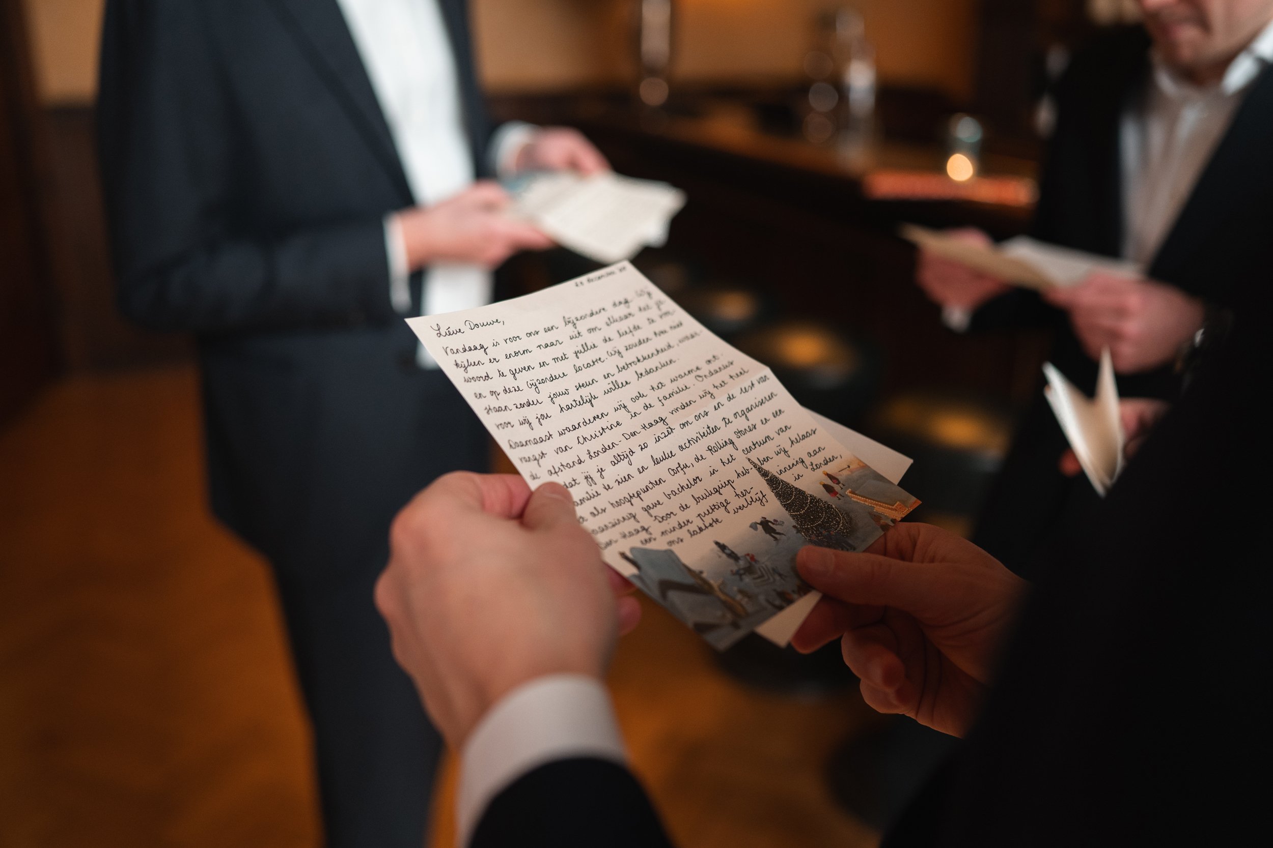 People in formal attire reading handwritten letters in a warmly lit room, possibly during a wedding or special event.