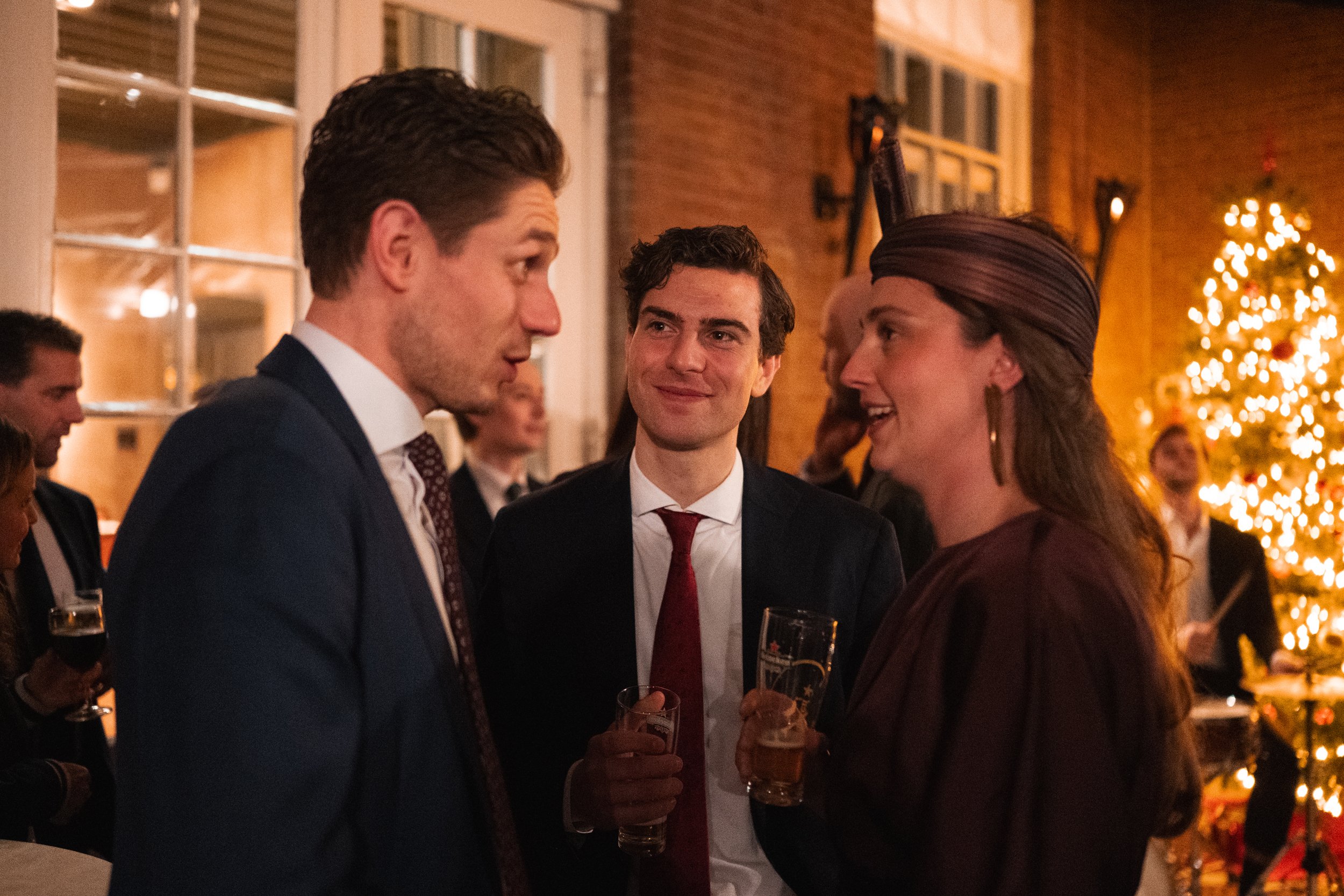 People at a holiday party socializing, with a decorated Christmas tree in the background.