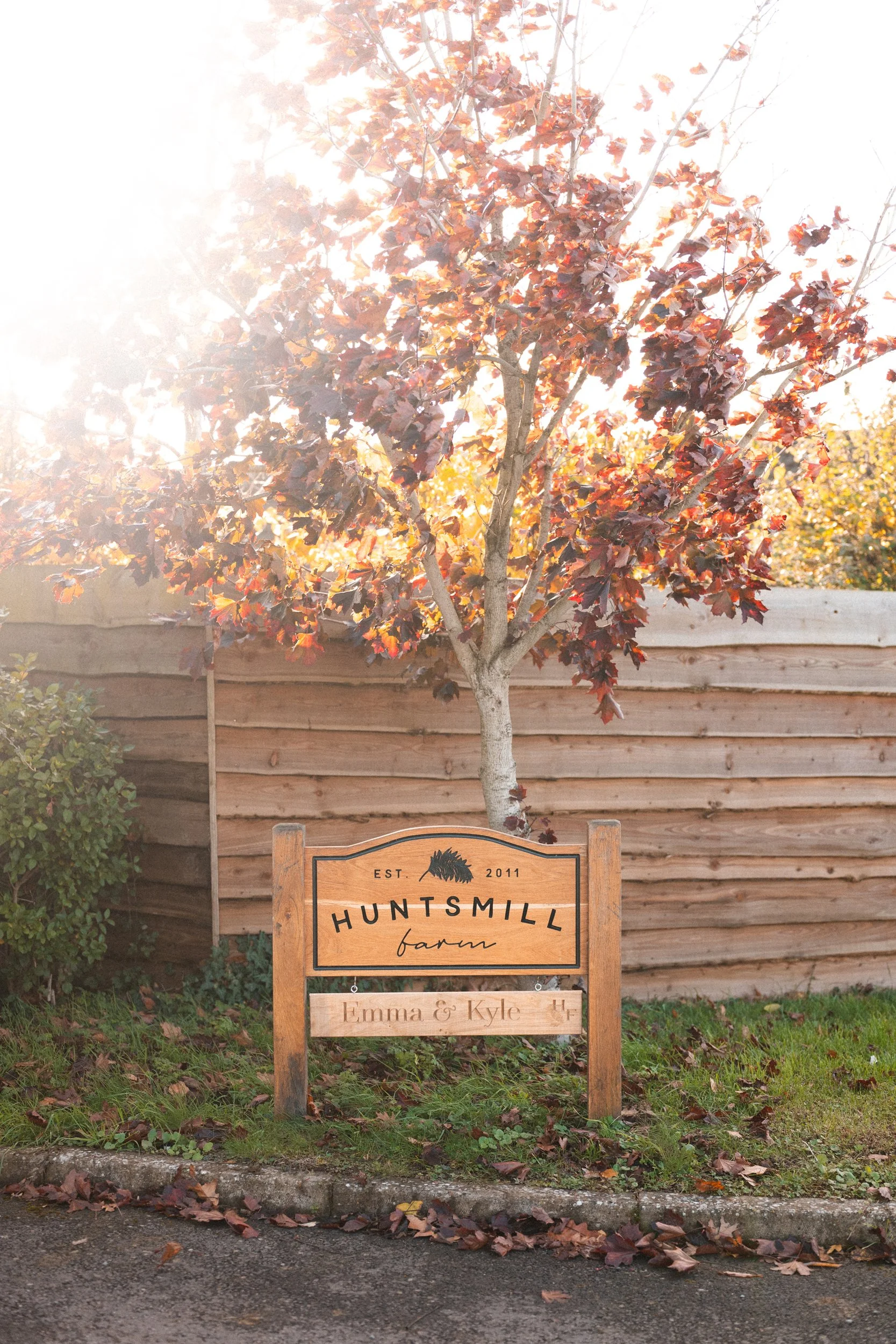 Wooden farm sign reading "HUNTSMILL farm" with a tree in the background and a wooden fence.