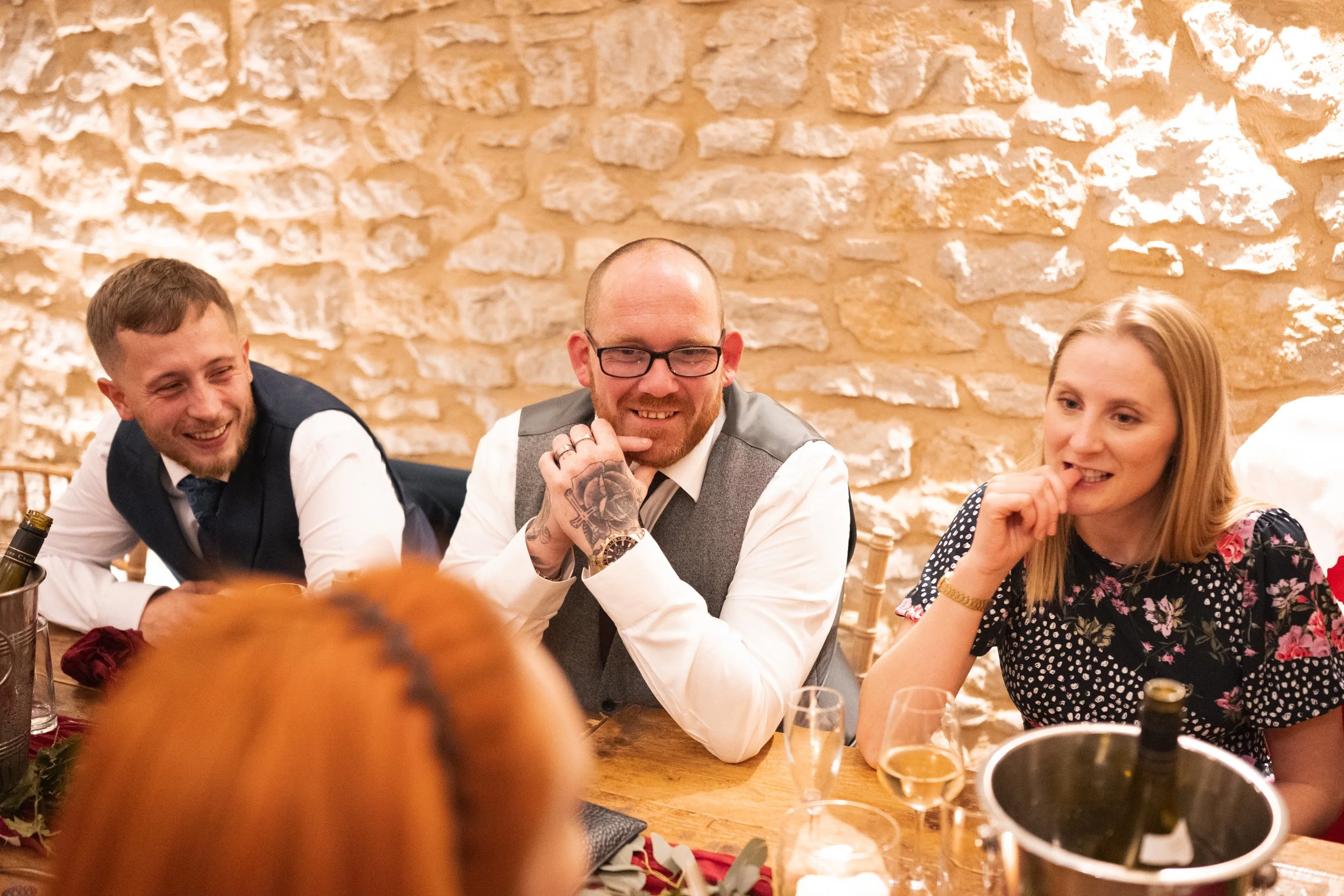 Three people sitting at a dining table with drinks, smiling and interacting in a cozy setting.