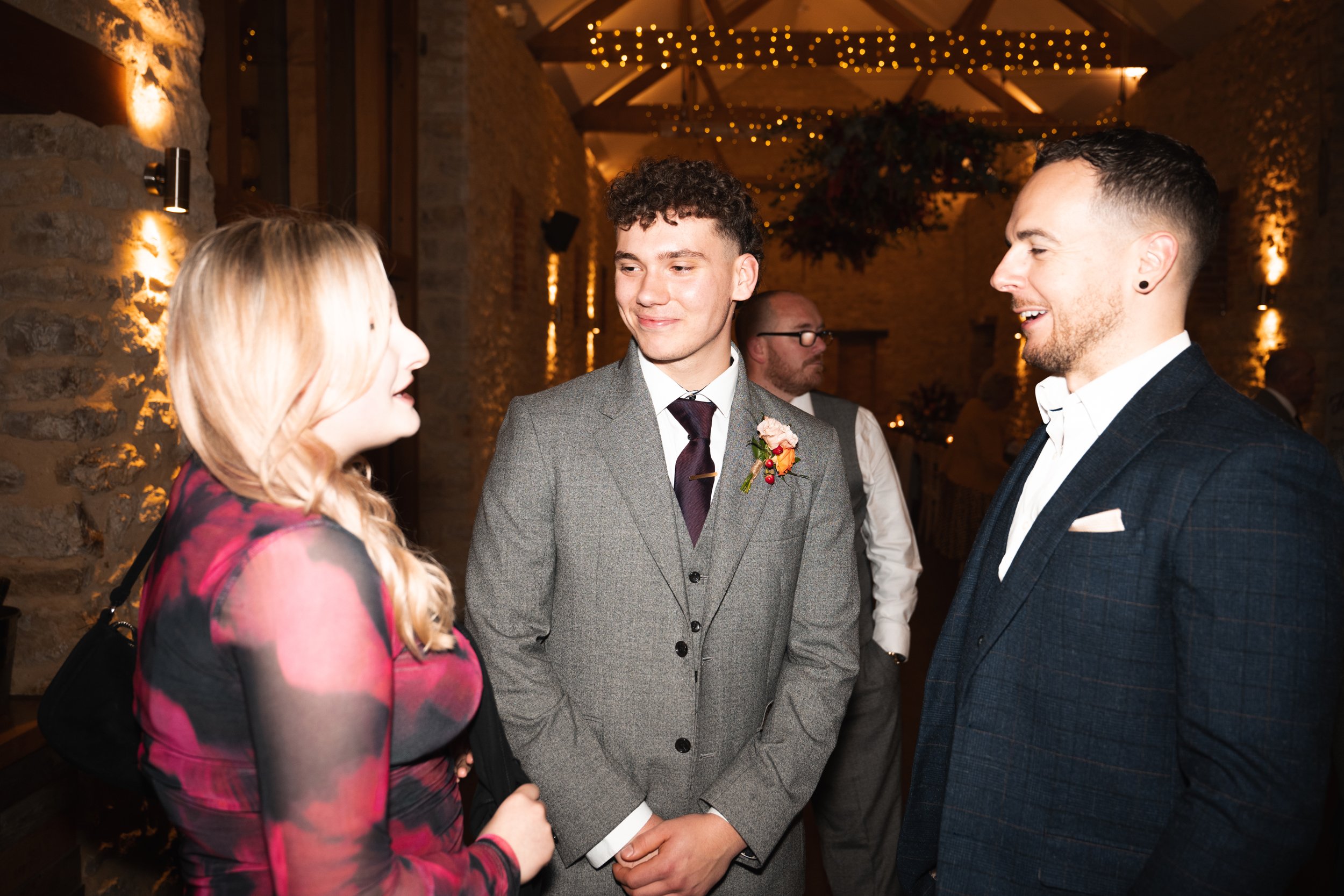 Three people engaged in conversation at an indoor event with warm lighting and decorative string lights.