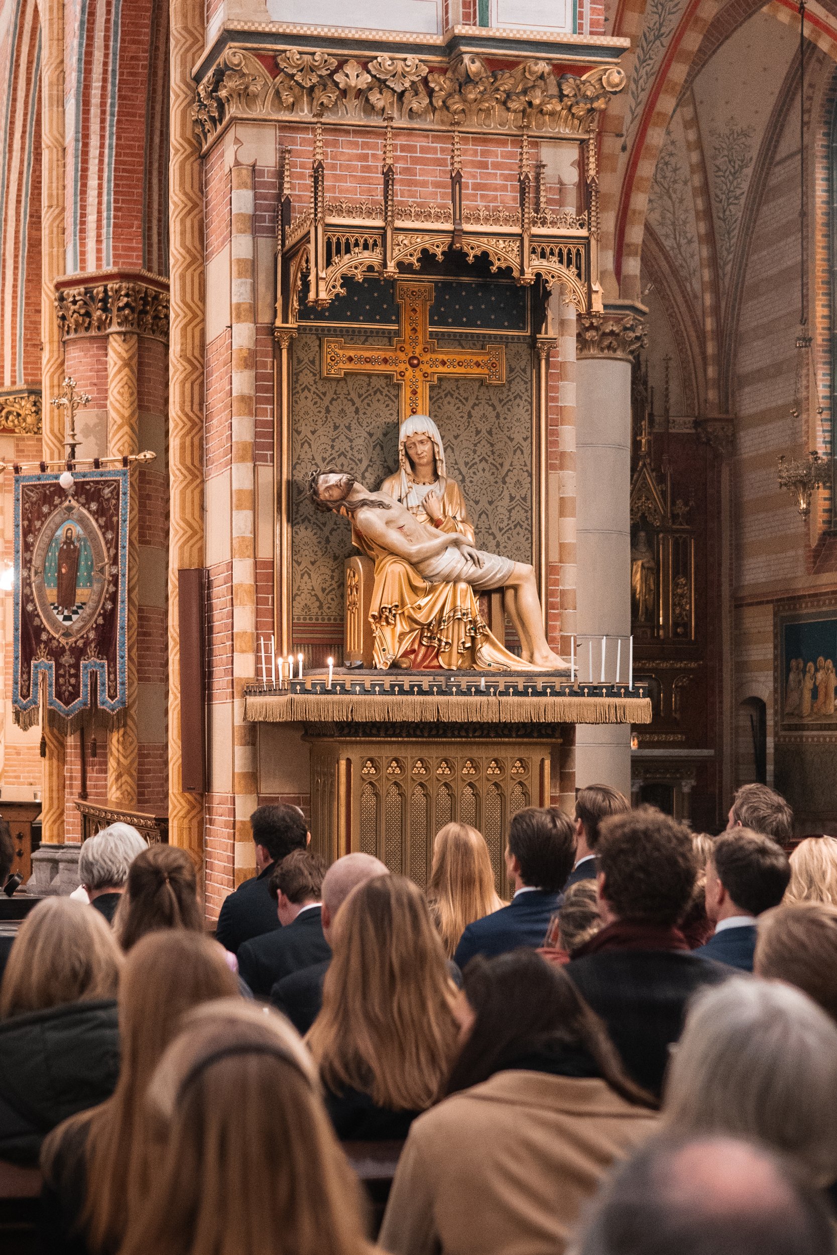 A church interior with a large religious sculpture of Jesus holding his body after crucifixion on a decorated altar, with worshippers seated and listening.