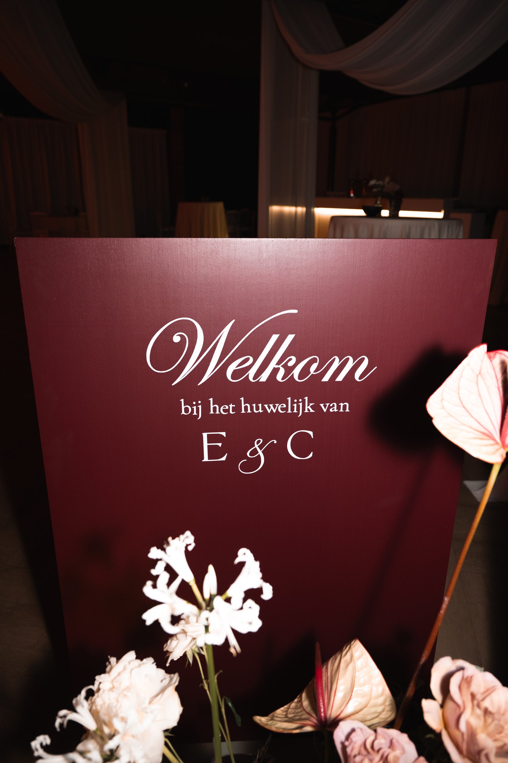 A welcome sign in Dutch at a wedding reception with floral decorations in the foreground.
