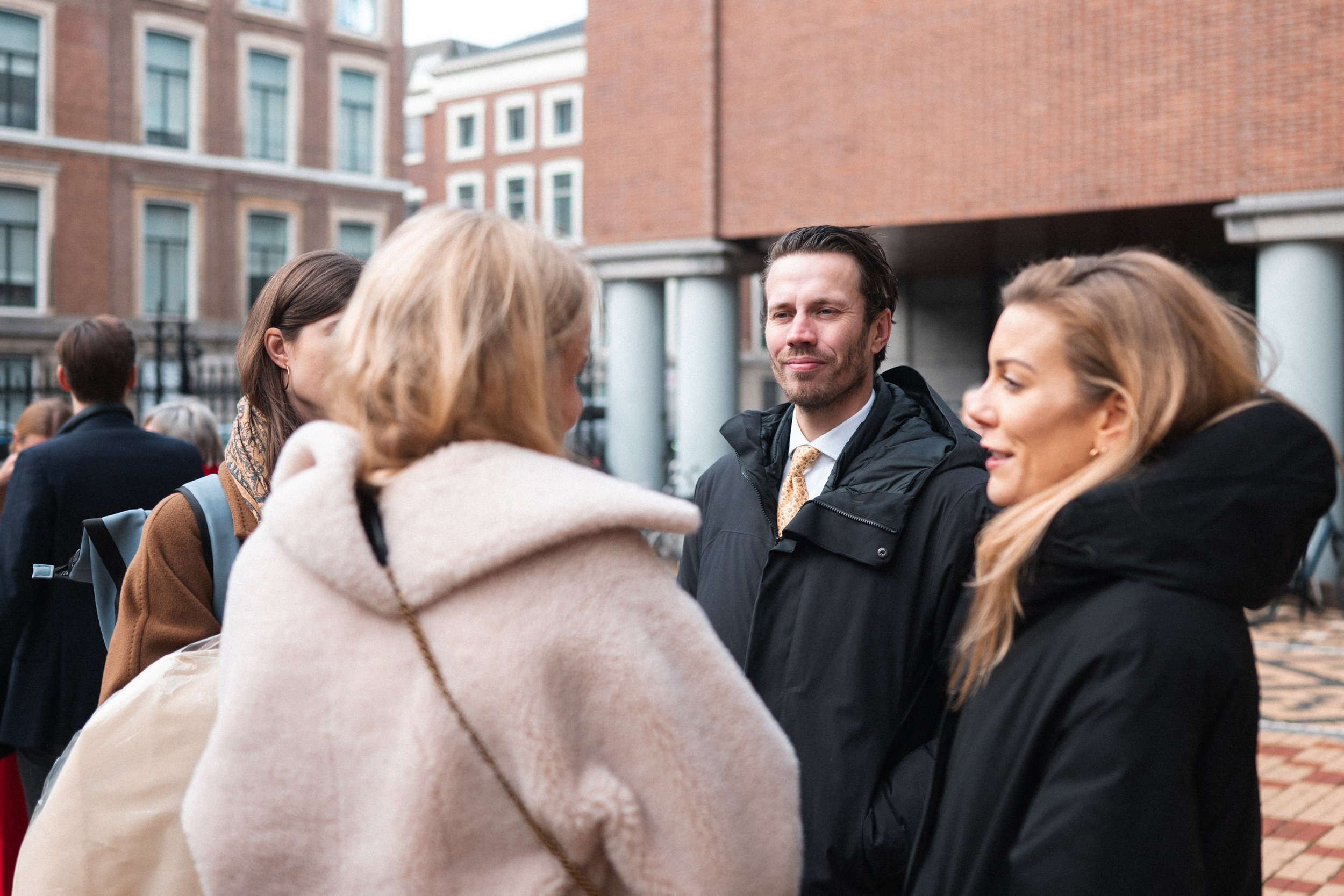 A group of four adults engaged in conversation outdoors in an urban area with brick buildings in the background.