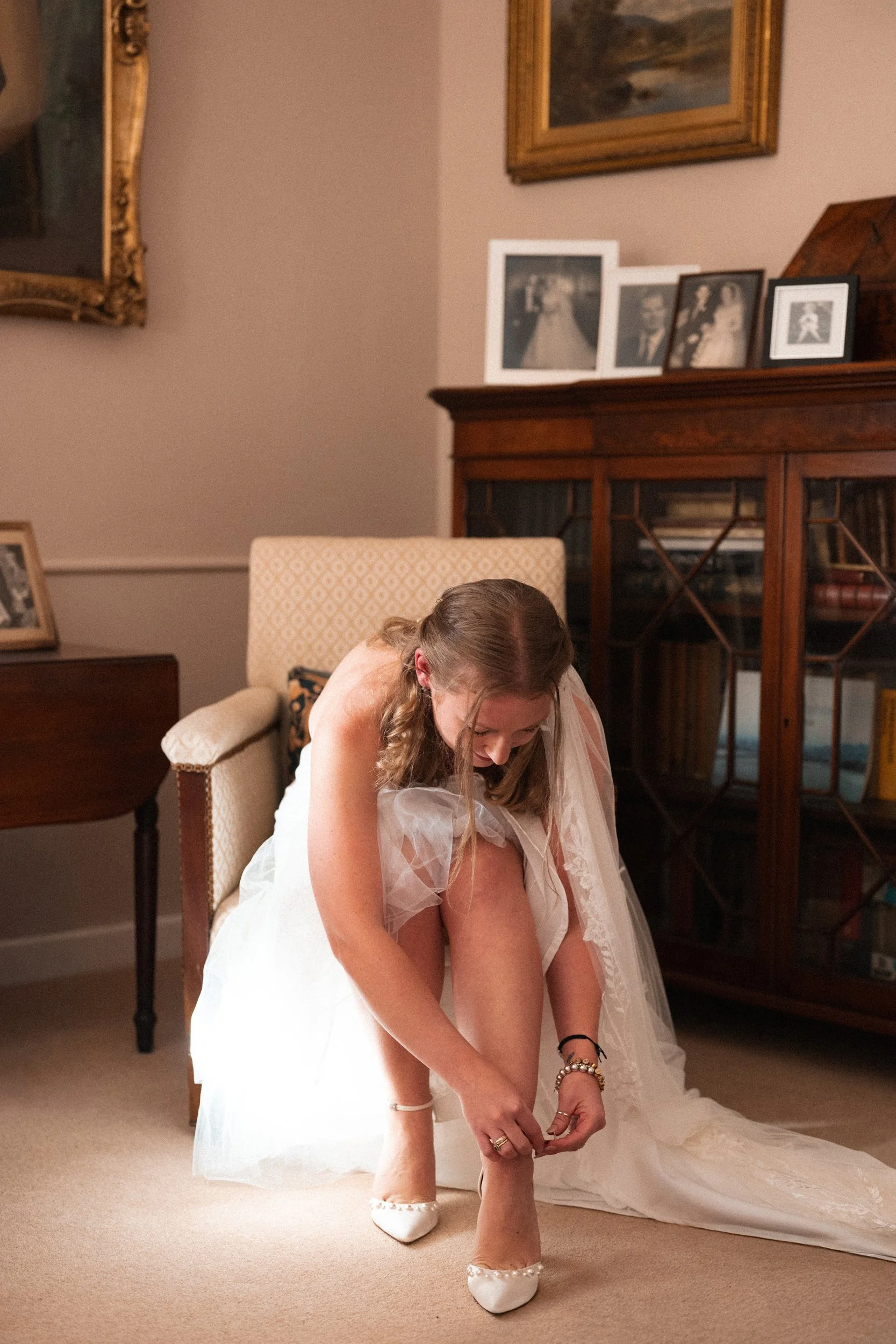 Bride in a wedding dress putting on her shoes in a cozy, vintage room.