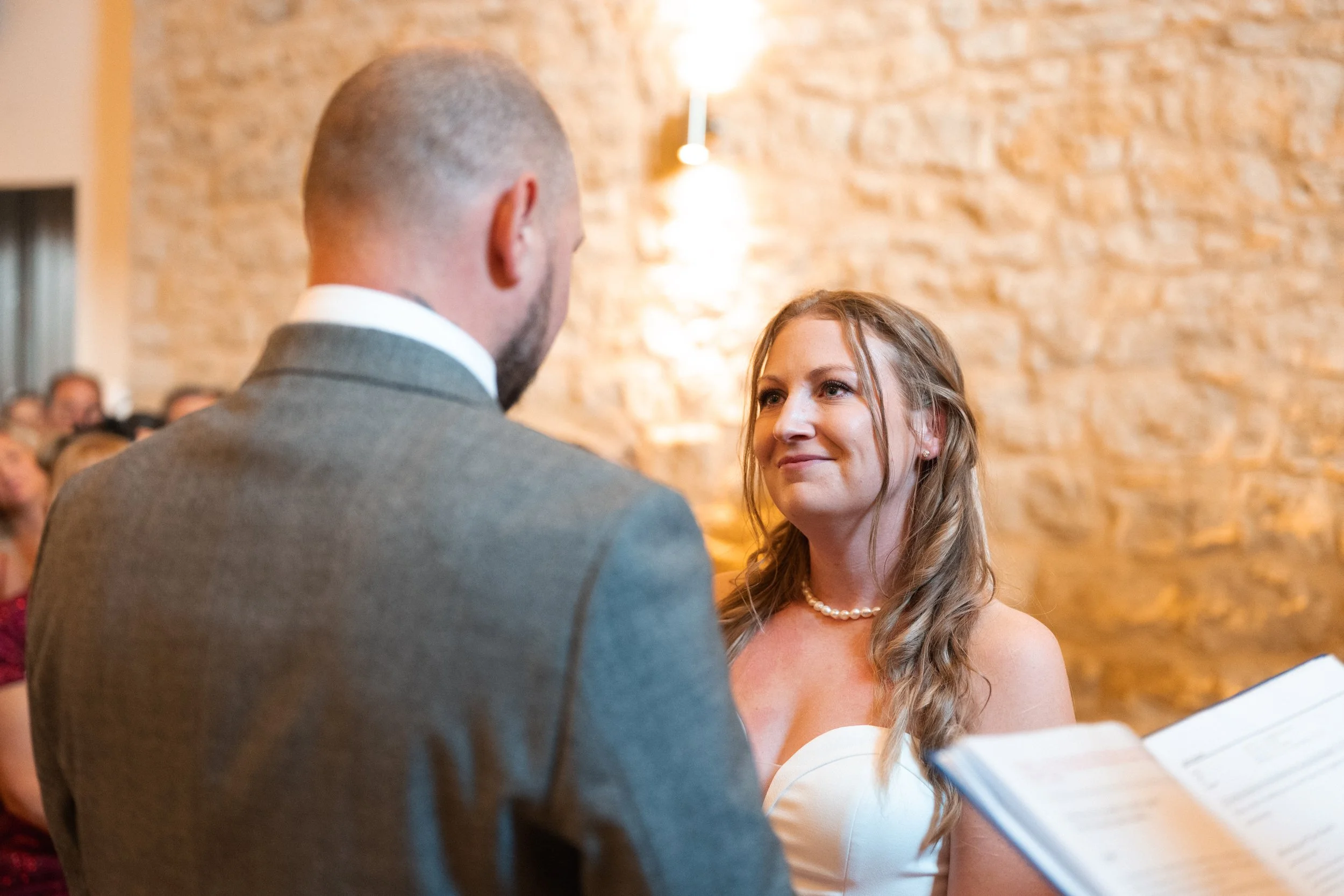 Bride and groom exchanging vows during a wedding ceremony indoors with a rustic brick wall background