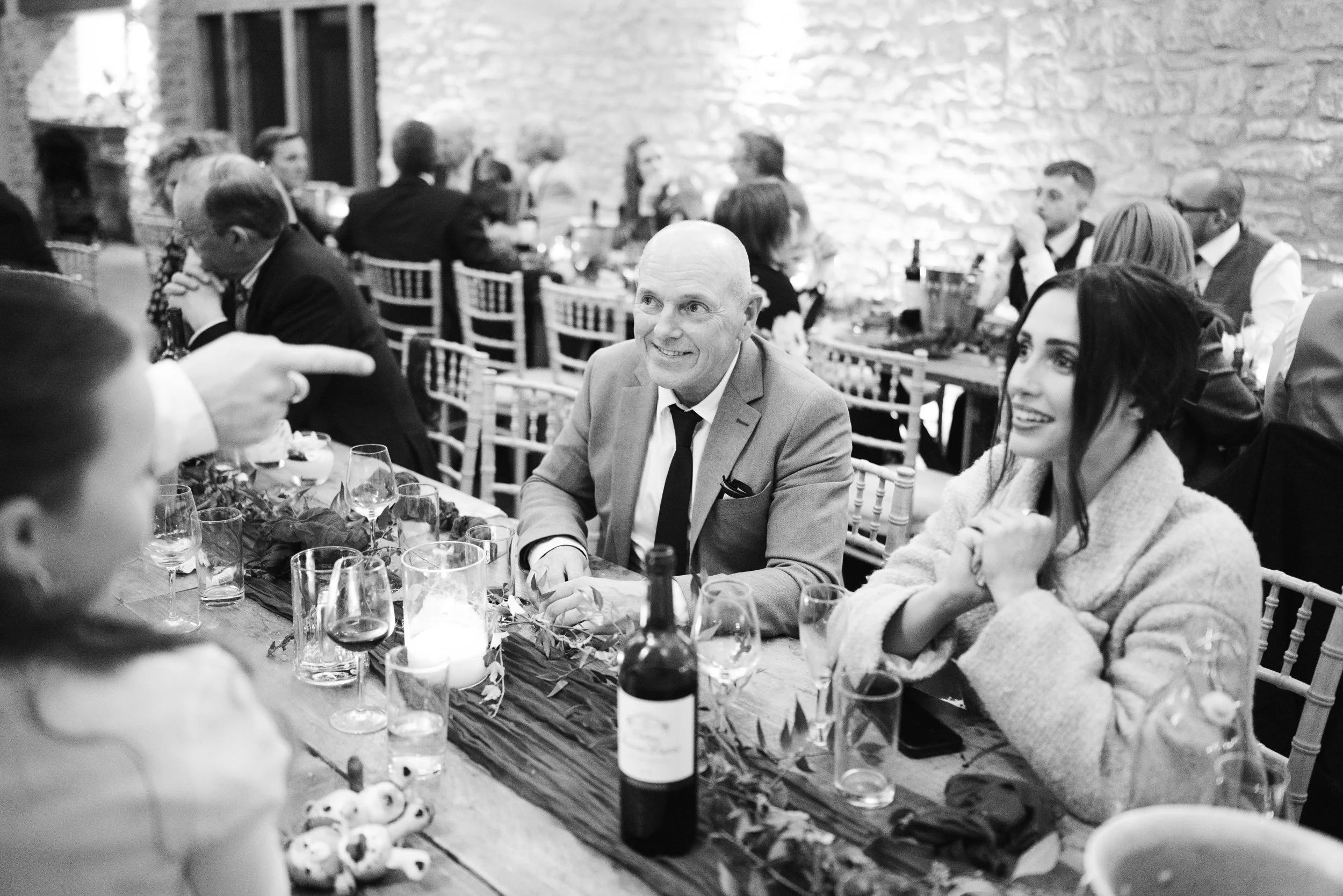People gathered around a decorated table at a social event or celebration, smiling and engaging in conversation in a rustic setting with exposed brick walls.