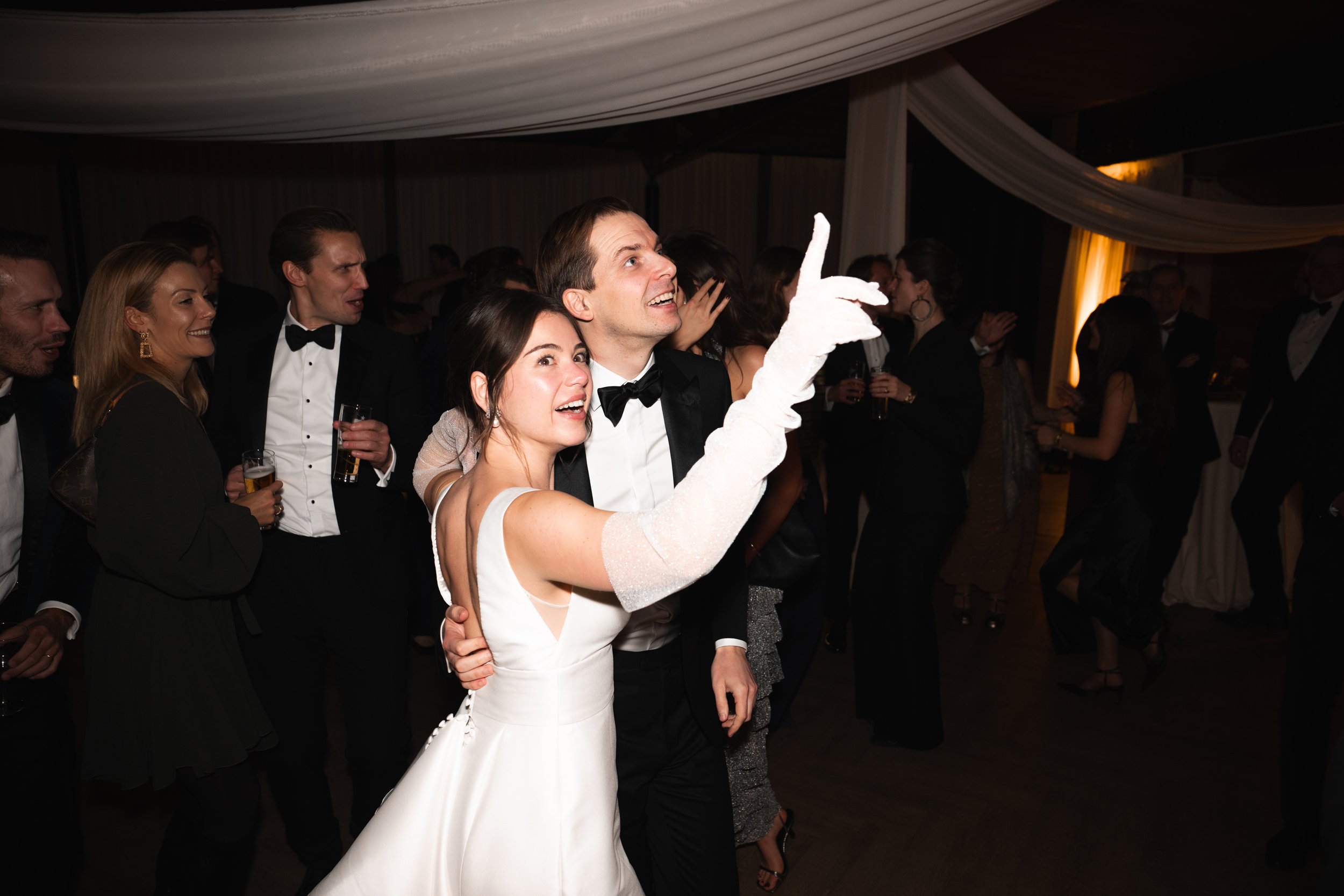 A bride and groom at a wedding reception dancing, surrounded by guests in formal attire.
