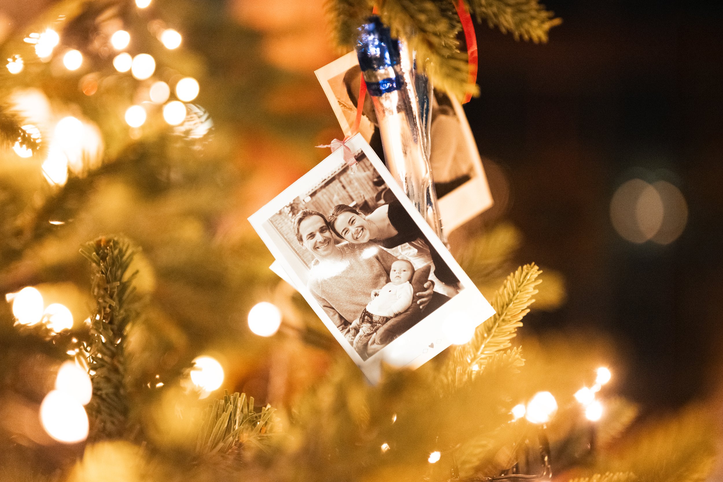 Photographs hanging on a decorated Christmas tree with glowing lights.