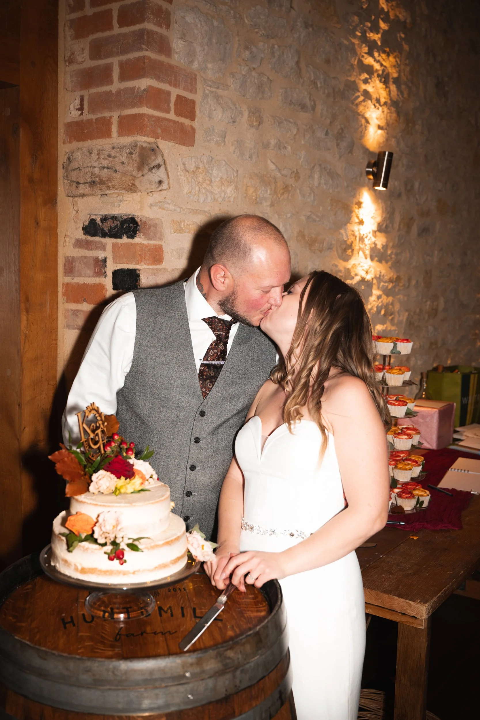 A couple in wedding attire sharing a kiss in front of a wedding cake at their celebration.