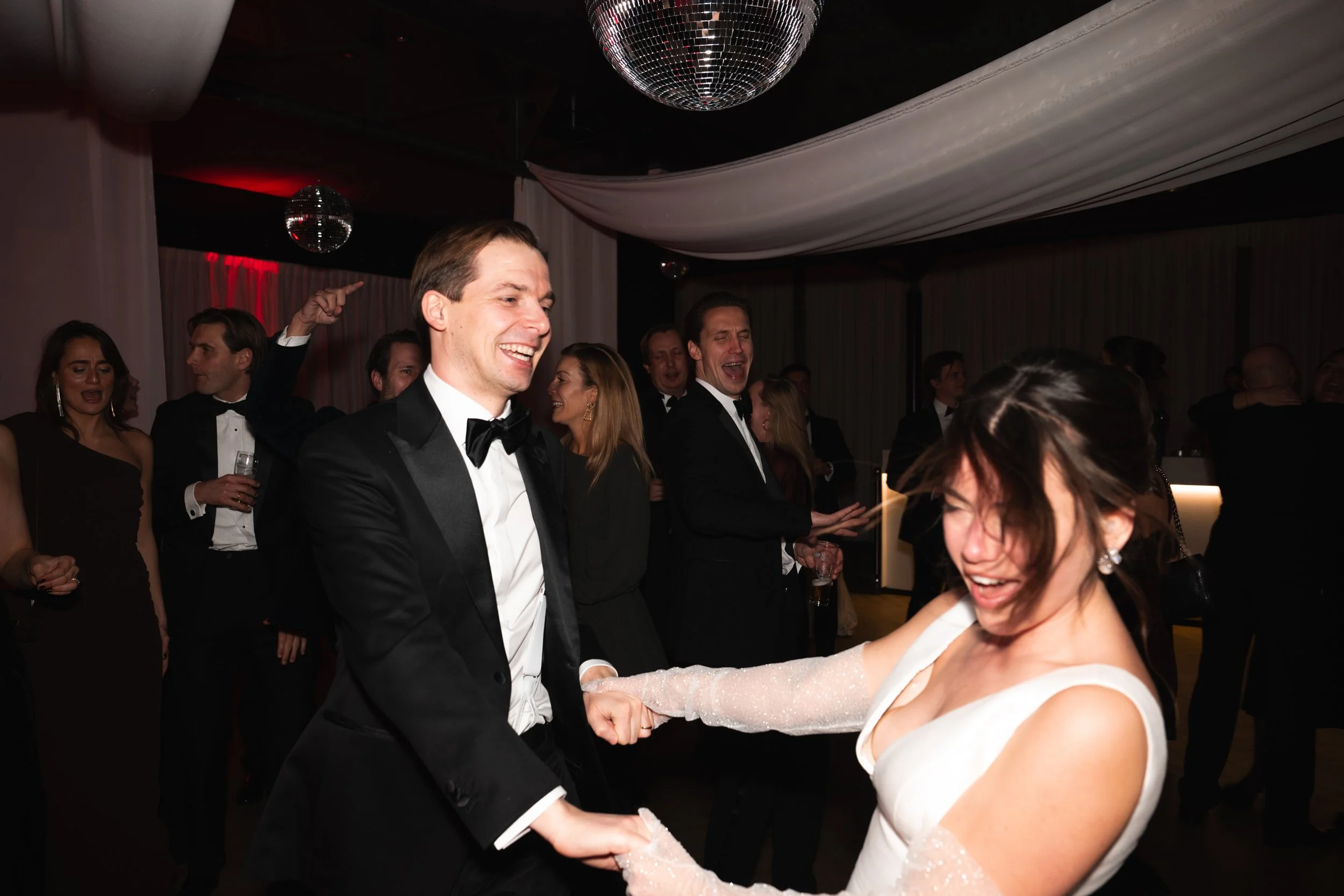 People dancing and celebrating at a formal event, including a couple in wedding attire dancing happily.