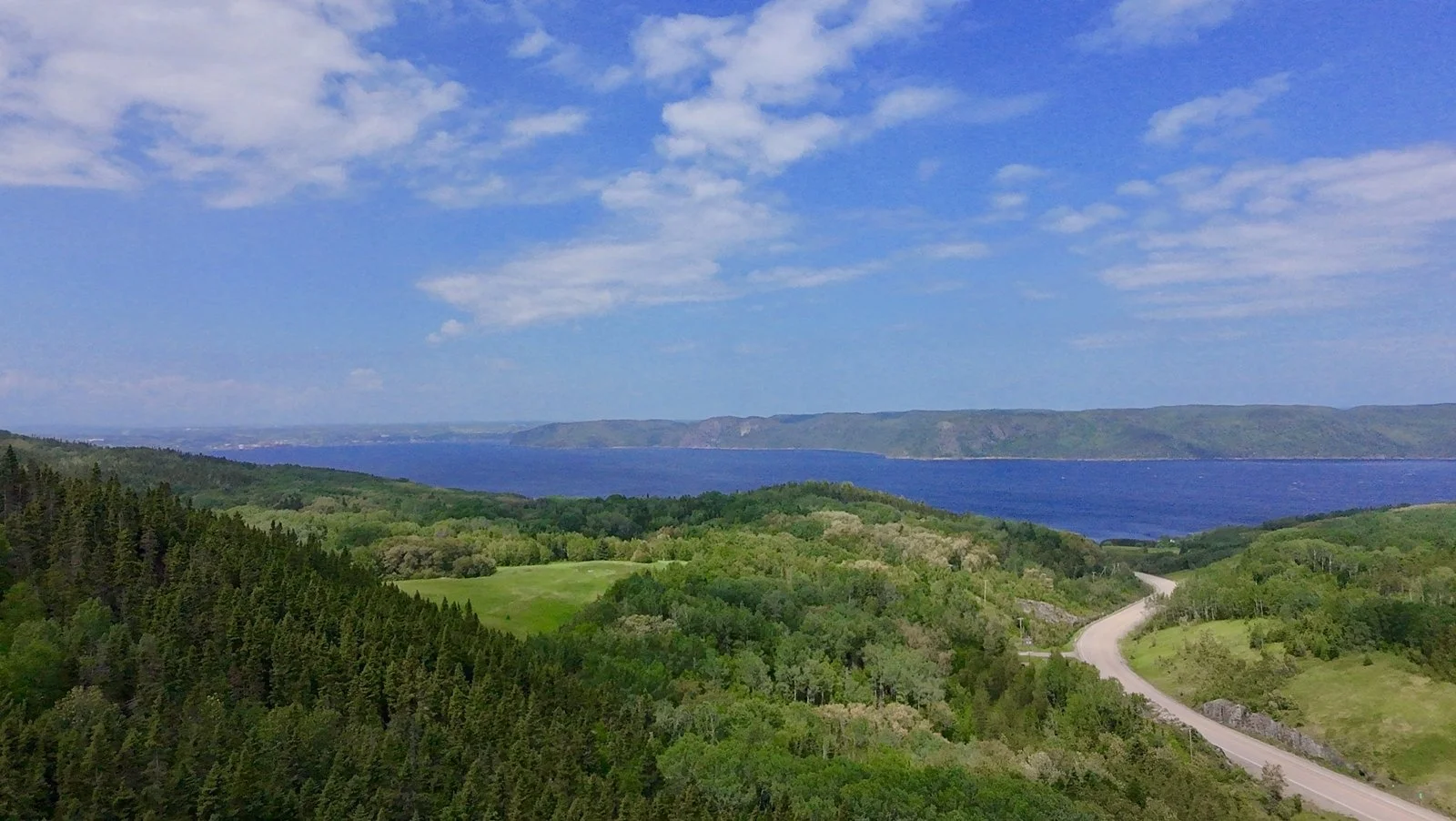 Paysage de collines verdoyantes avec lac et ciel bleu avec quelques nuages.