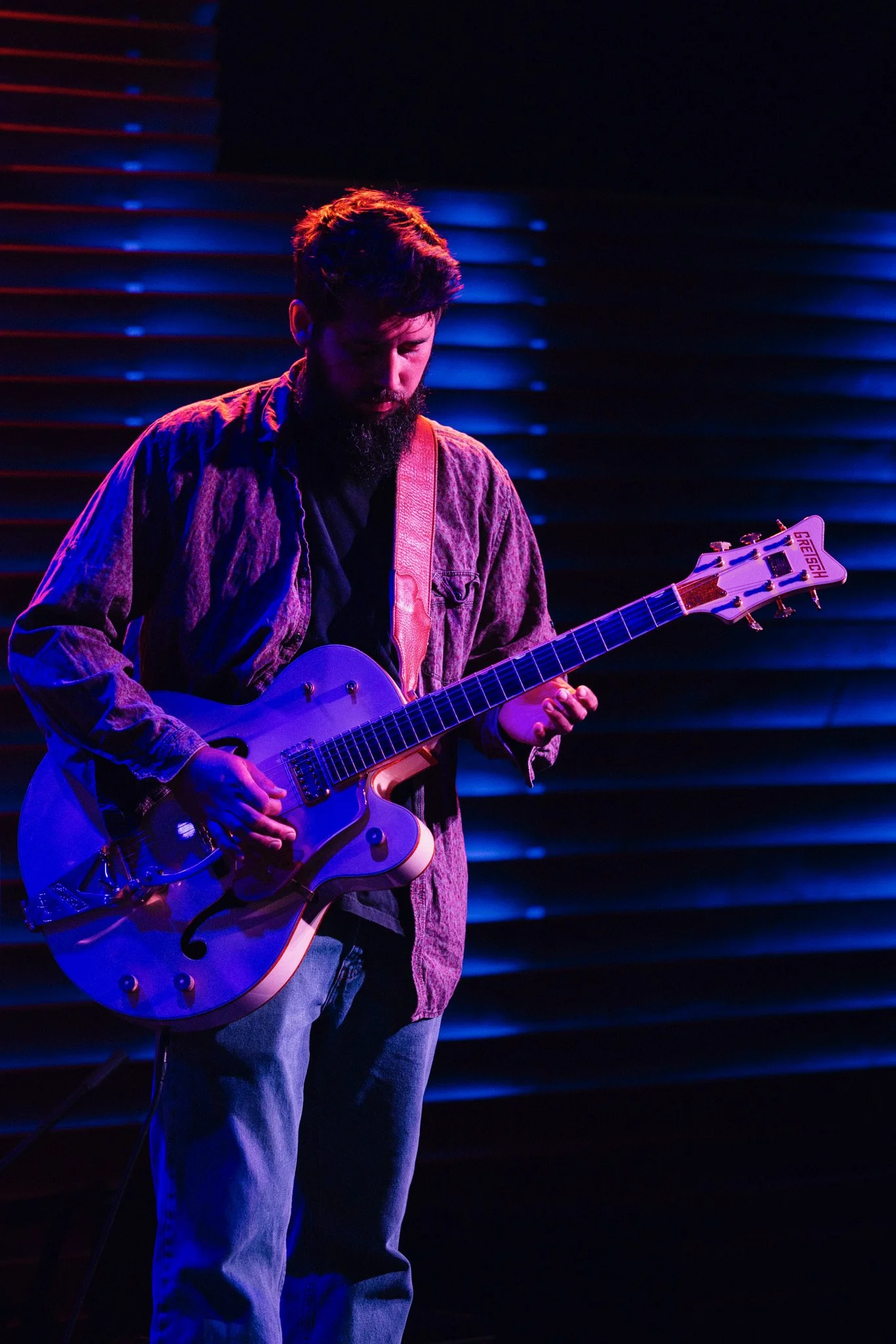 A man playing an electric bass guitar on stage with a neon-lit backdrop that reads 'Vertical.'