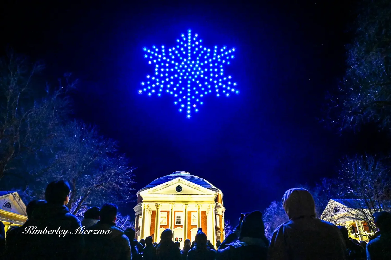 A blue drone snowflake above UVA’s illuminated Rotunda and spectators at Lighting of the Lawn