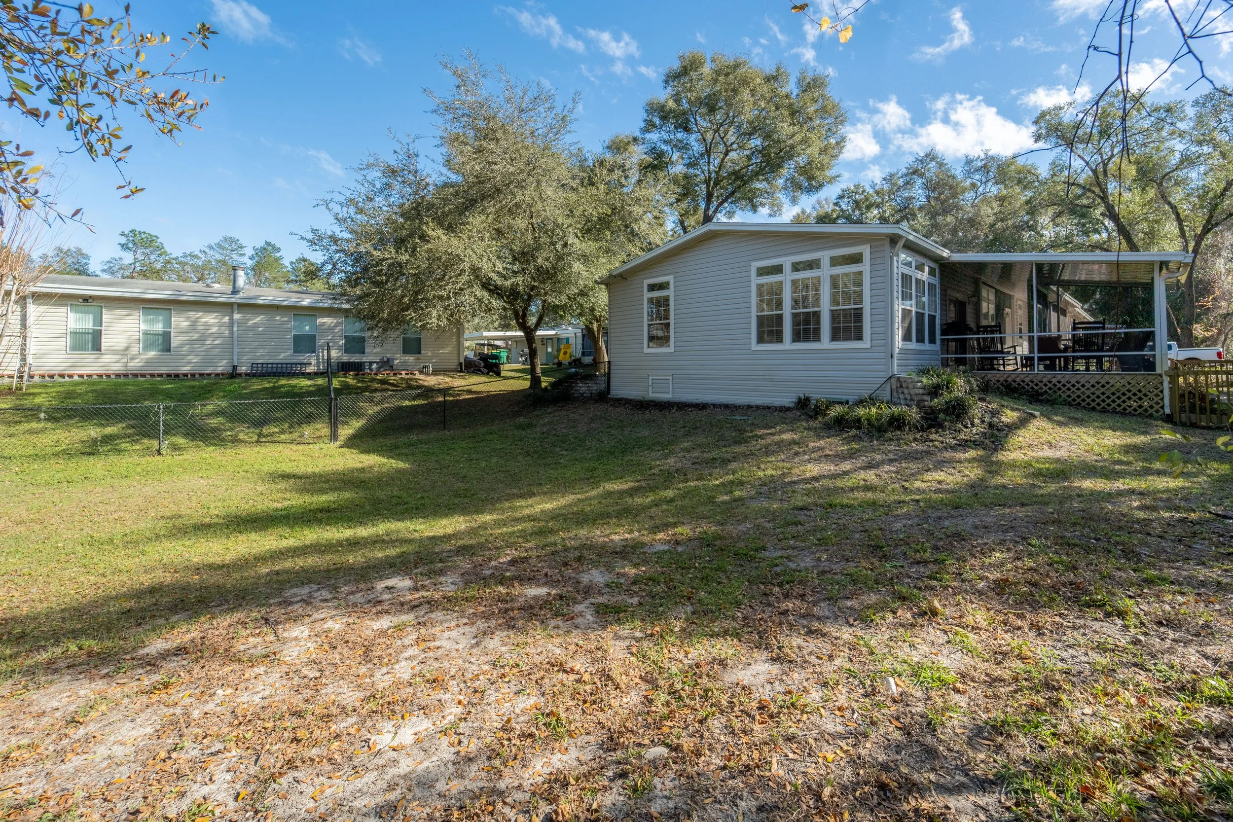 Backyard with a grassy lawn, trees, and houses under a blue sky with clouds.