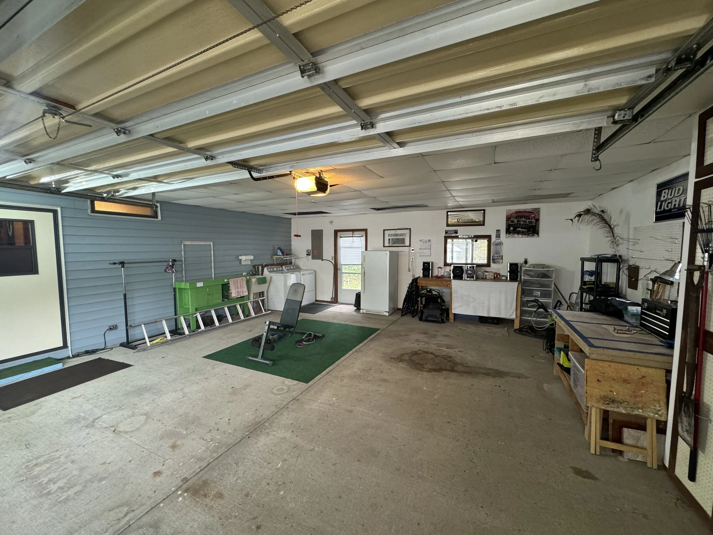 A spacious garage with a workout area, laundry machines, a workbench, and storage shelves.