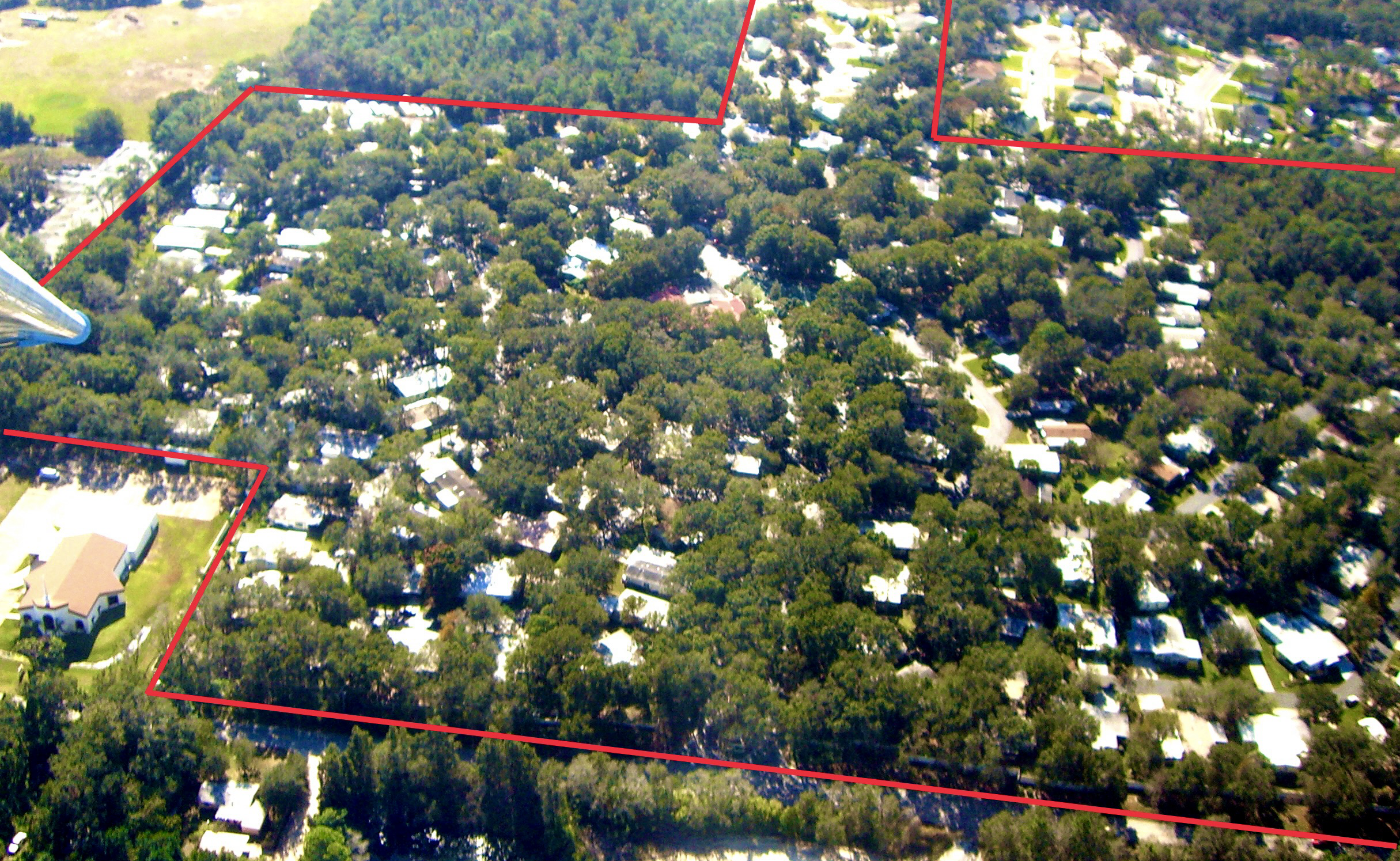 Aerial view of a residential neighborhood with numerous houses surrounded by trees, with red boundary lines outlining a specific property area.