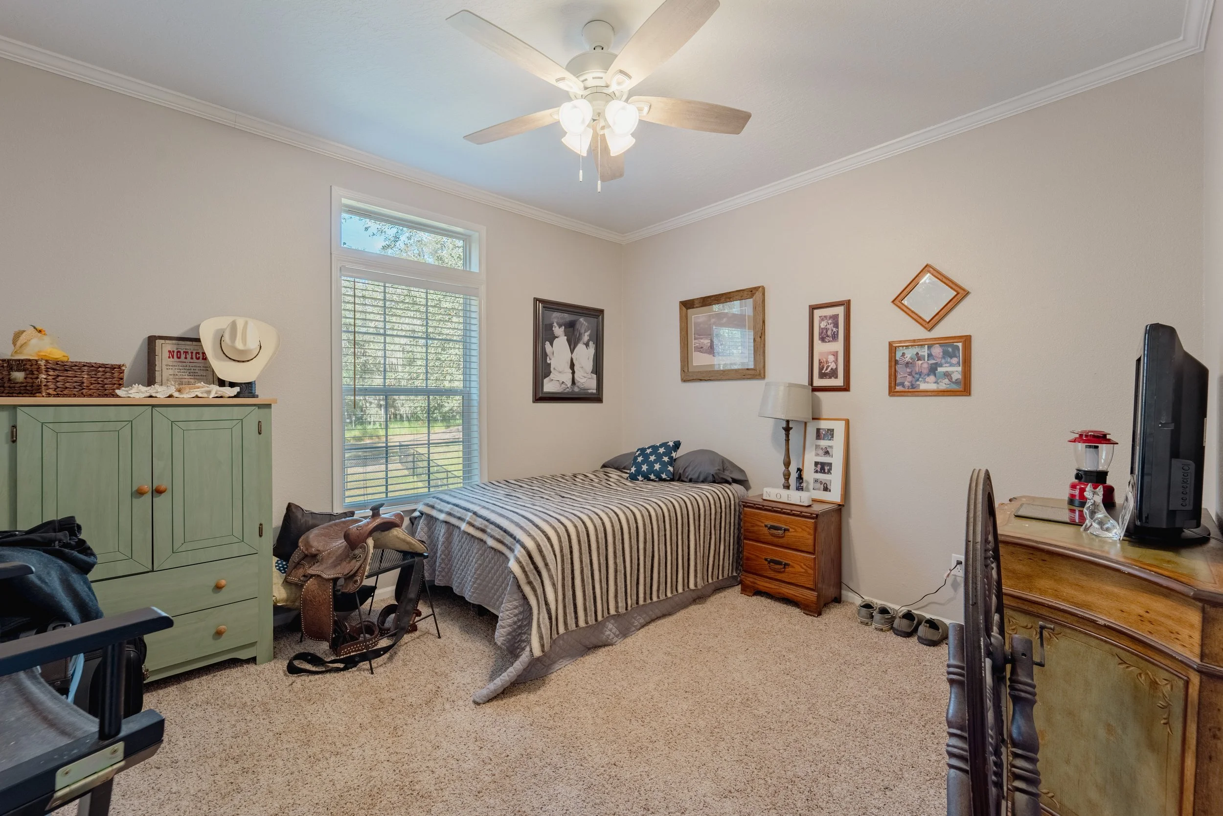 A bedroom with a bed, dresser, and various decor including wall art and a ceiling fan.