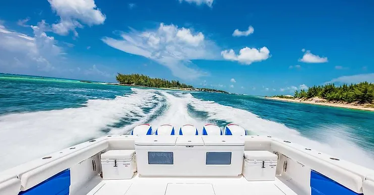 View from the back of a motorboat speeding on clear blue water near a small island with trees, under a partly cloudy sky.