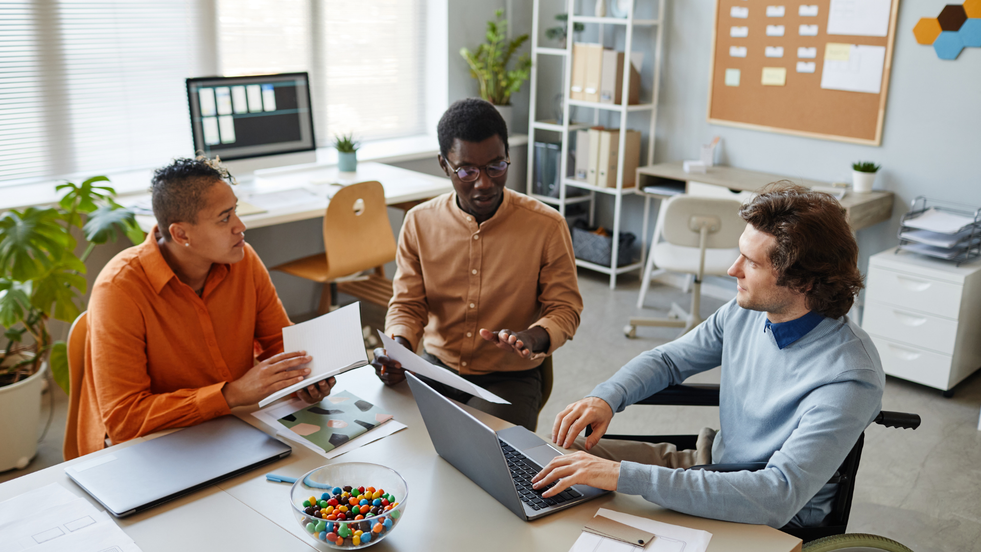 a group of colleagues gather around a table, discussing and reviewing printed files.