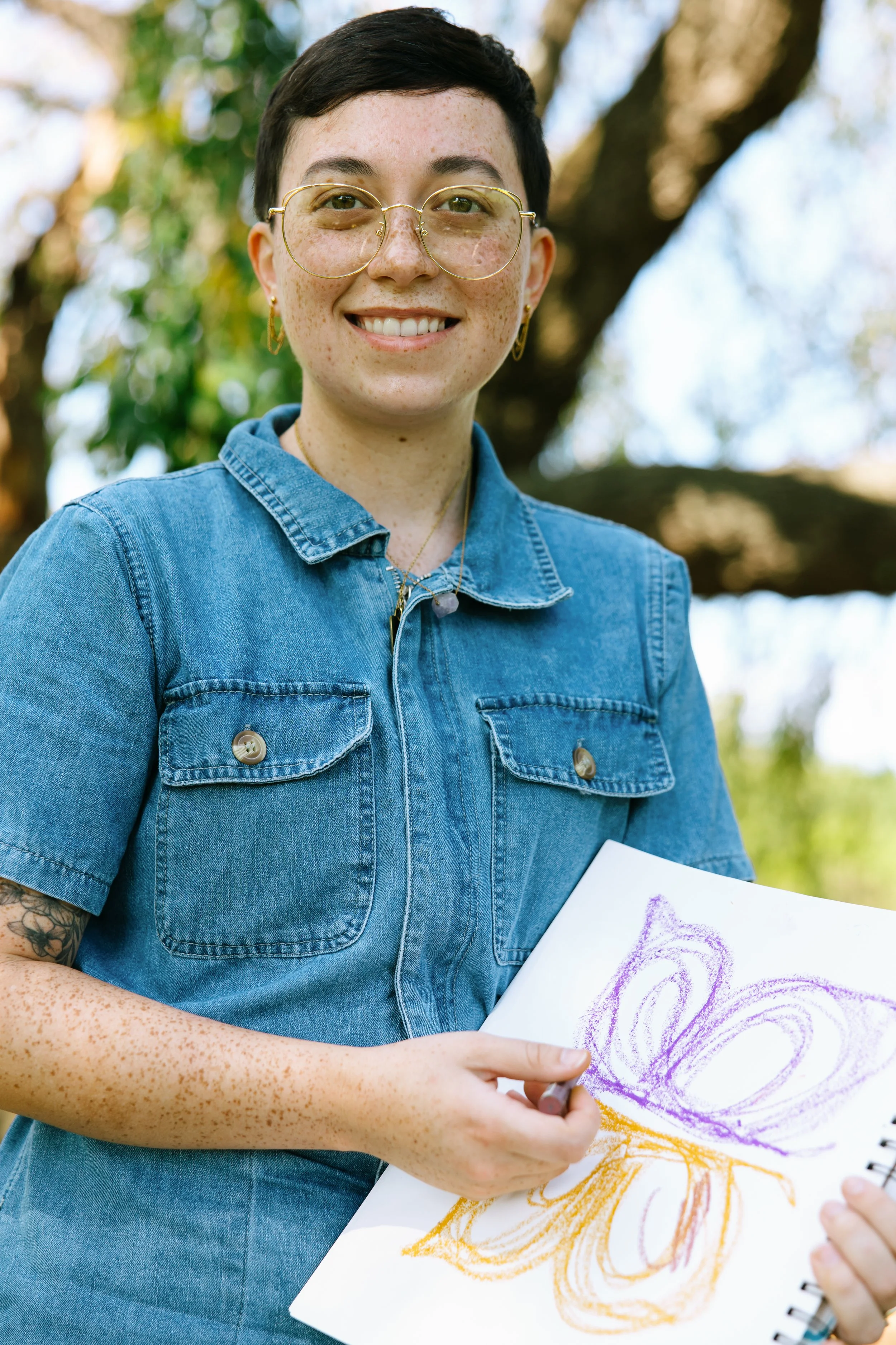 Nonbinary art therapist Kristy Leone drawing a butterfly outdoors with nonbinary pride colors.