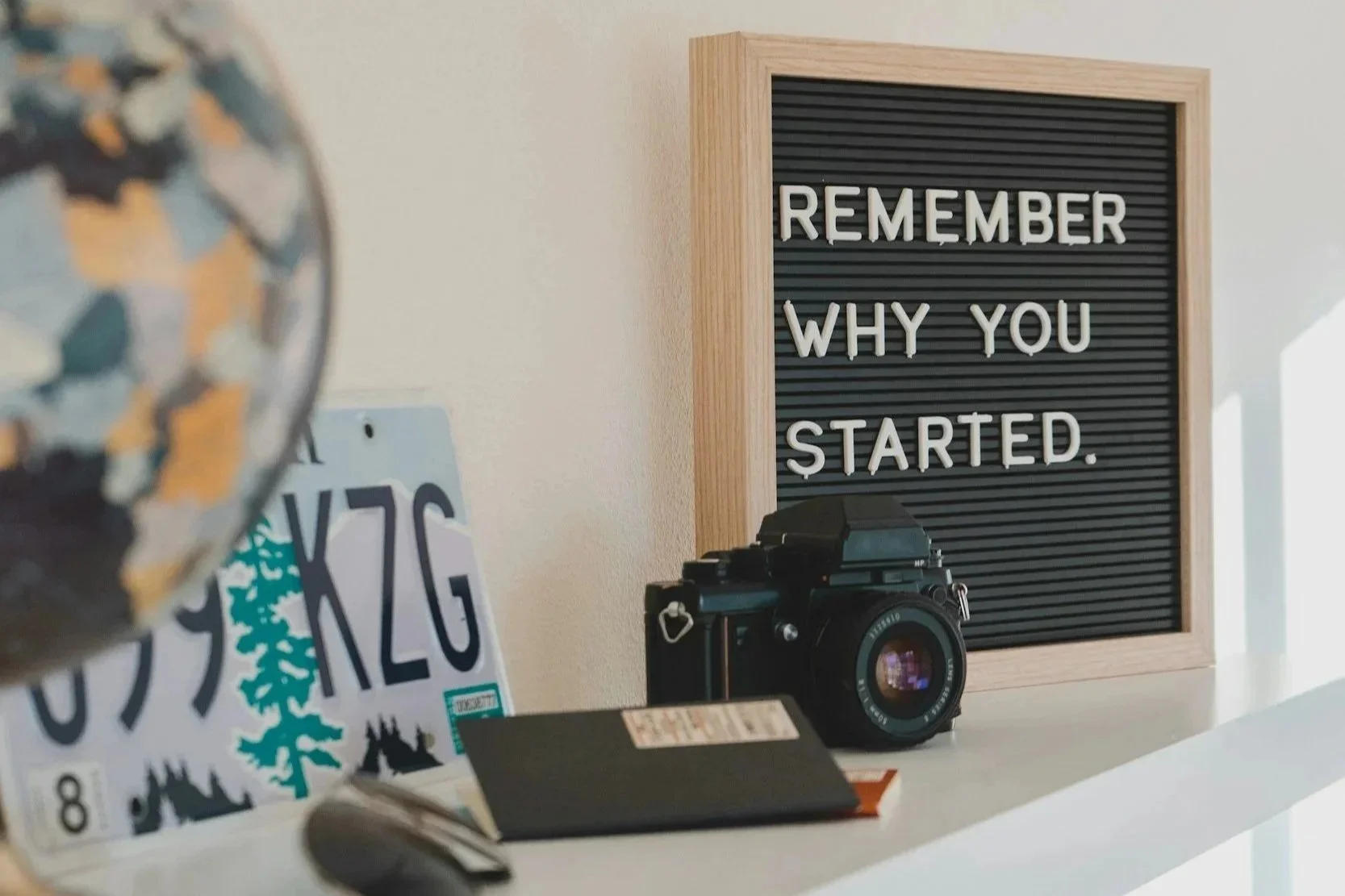 Workspace shelf with a vintage camera and a letter board reading “Remember why you started.”
