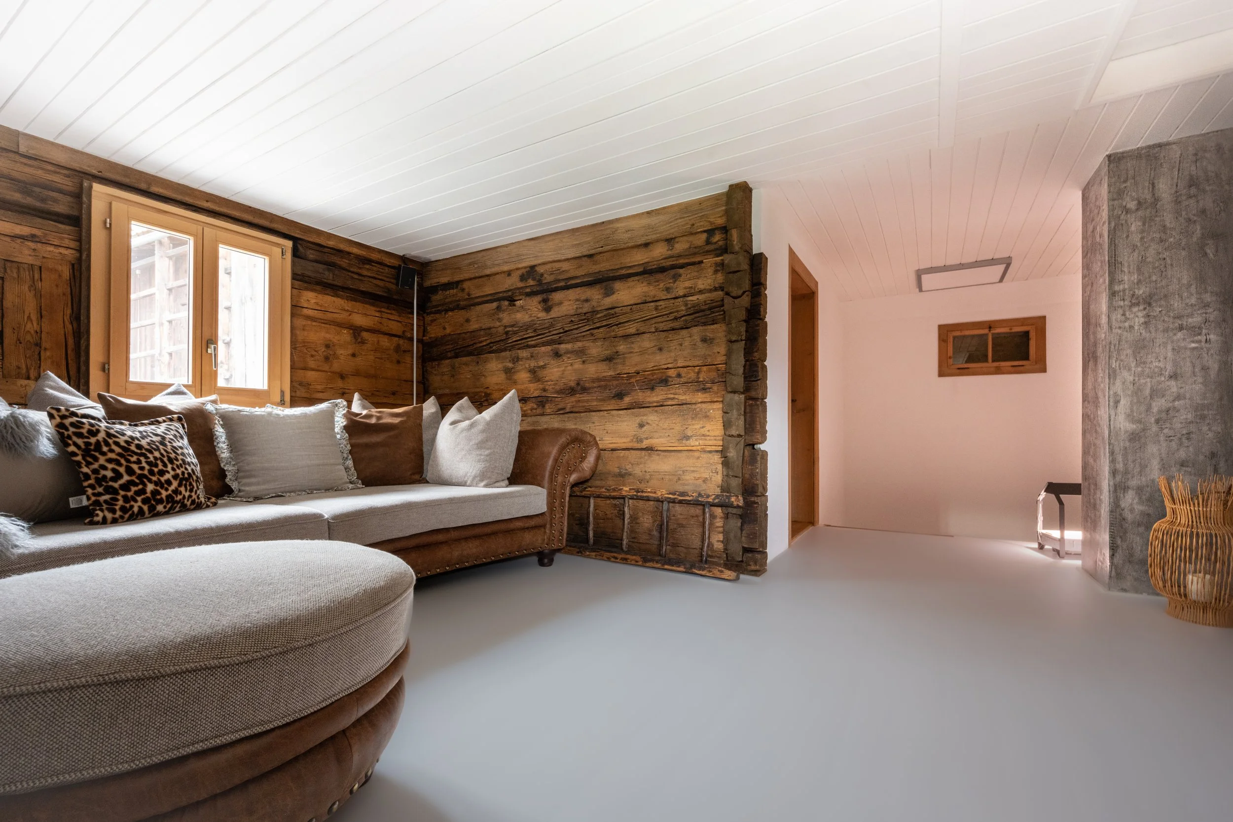 Wohnzimmer mit rustikalen Holz-Wänden, weißen Boden, vielen Kissen auf einer Couch, kleine Fenster, moderner Innenarchitektur.