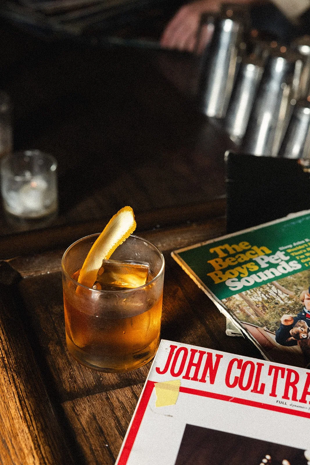 A glass of iced tea with a lemon wedge on a wooden table, next to magazines and a candle in a small glass holder.