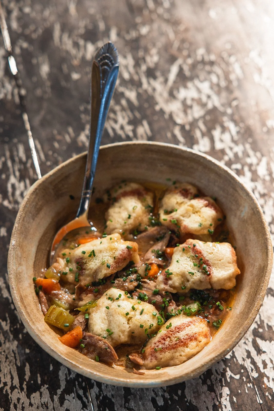 Bowl of chicken and vegetable pot pie stew with herbs, served in a rustic bowl on a wooden surface.