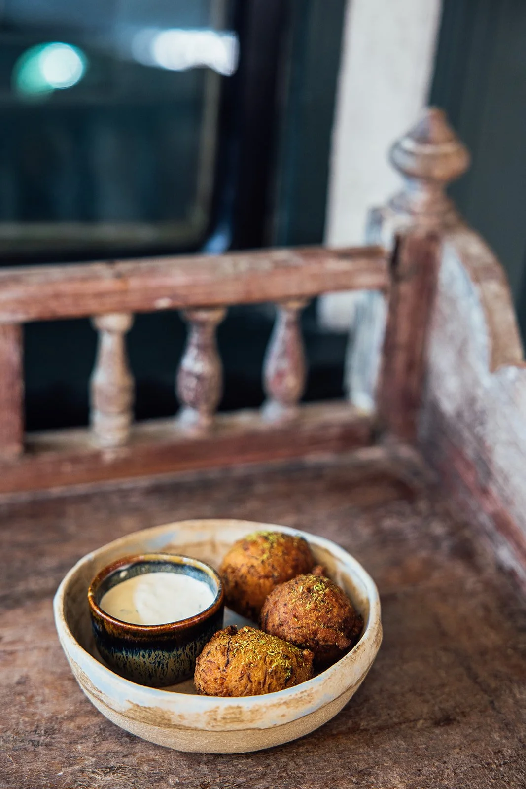 A bowl of three falafel balls with a small dish of white dipping sauce on a rustic wooden table.