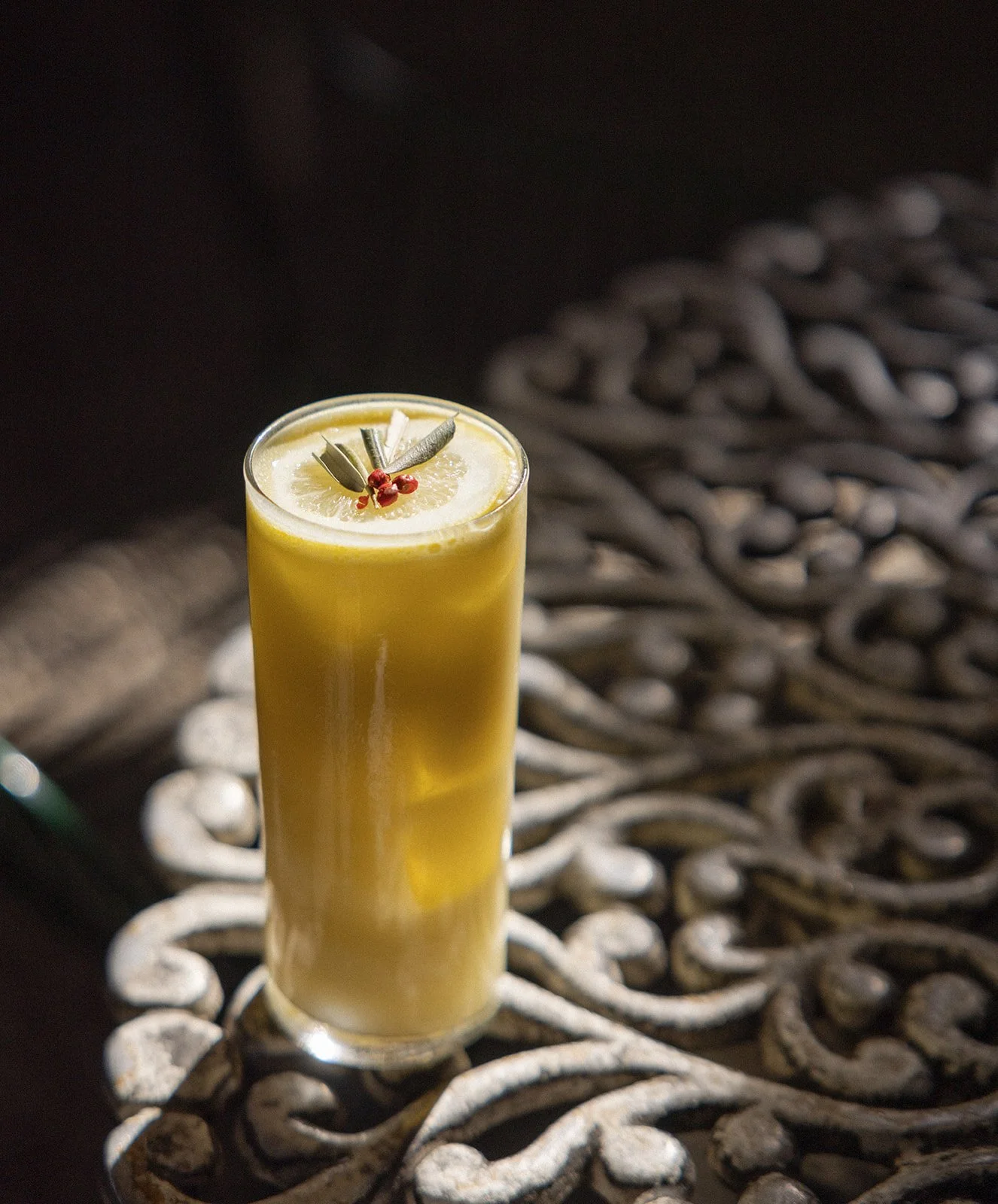 A tall glass of lemon and honey drink garnished with lemon slices and herbs, placed on an ornate metal table.