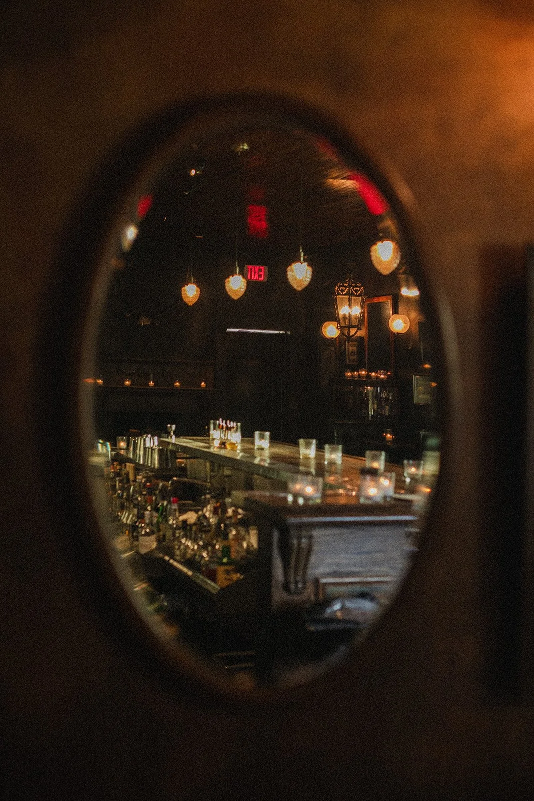 A dimly lit bar seen through a small oval mirror, with hanging heart-shaped lights and bottles behind the counter.