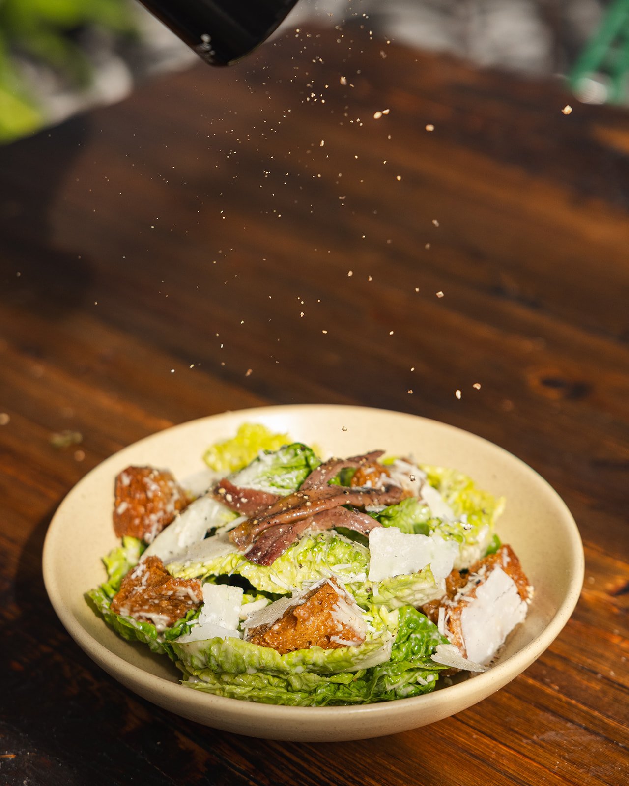 Caesar salad with croutons, bacon, and parmesan cheese on a beige bowl on a wooden table