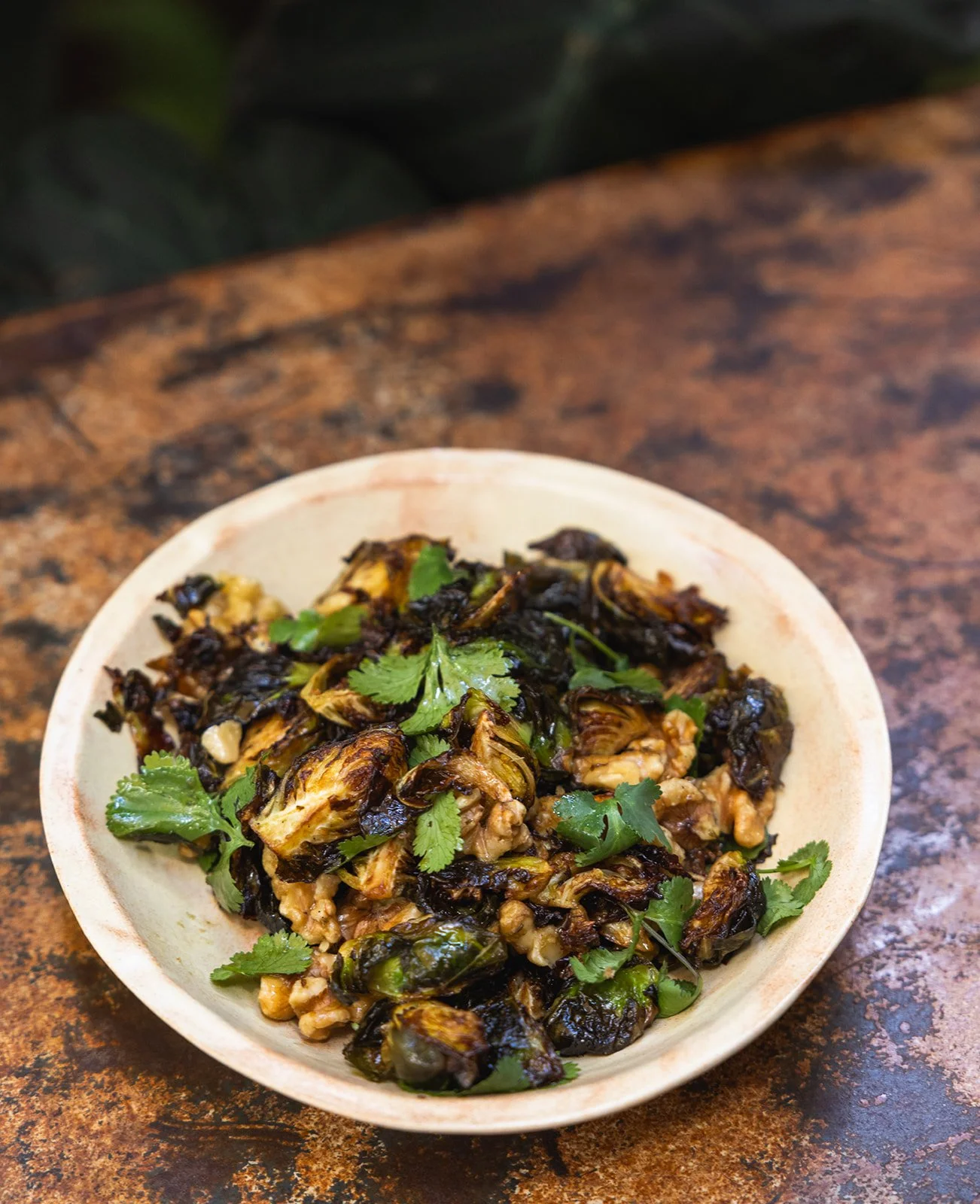 A bowl of roasted Brussels sprouts garnished with cilantro on a wooden table.