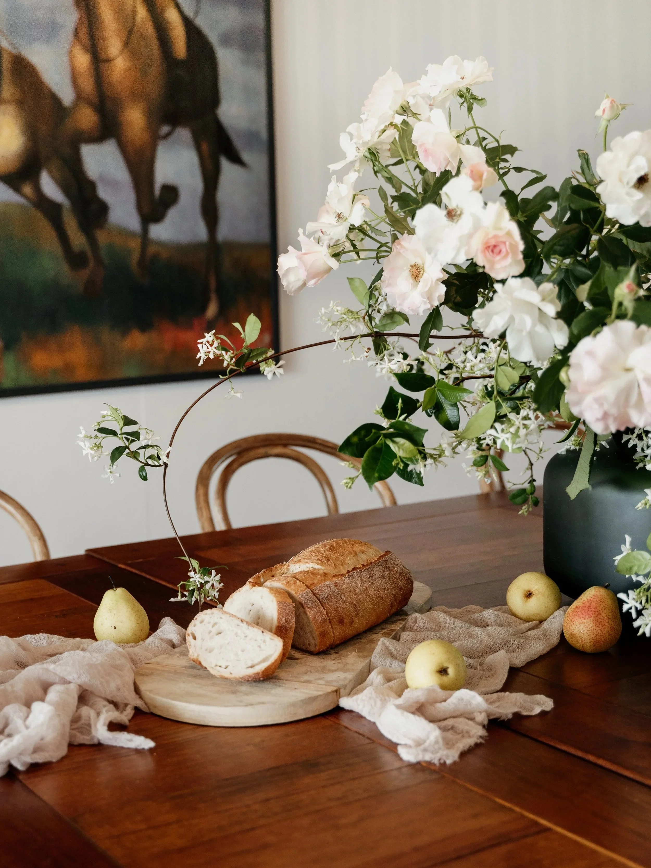 Interior Styling Oversized Arrangement Of Roses And Flowers Centre Piece On Dining Room With Fresh Bread And Artwork Hung As Feature