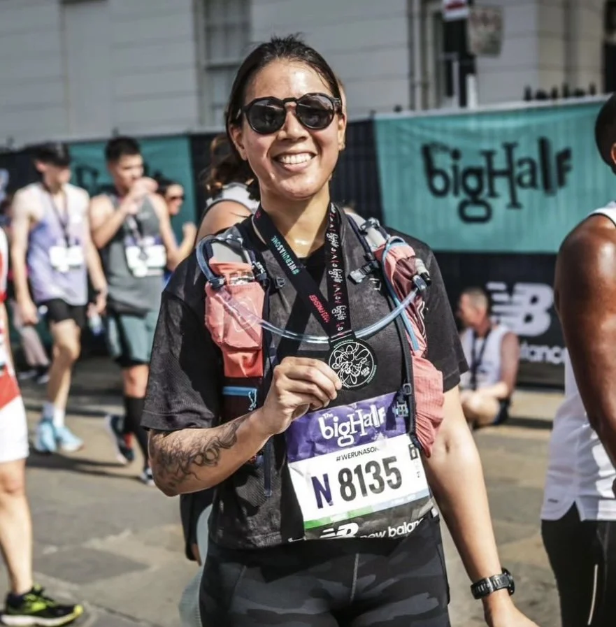 Woman wearing sunglasses and a race bib, holding a finisher medal at a running event.