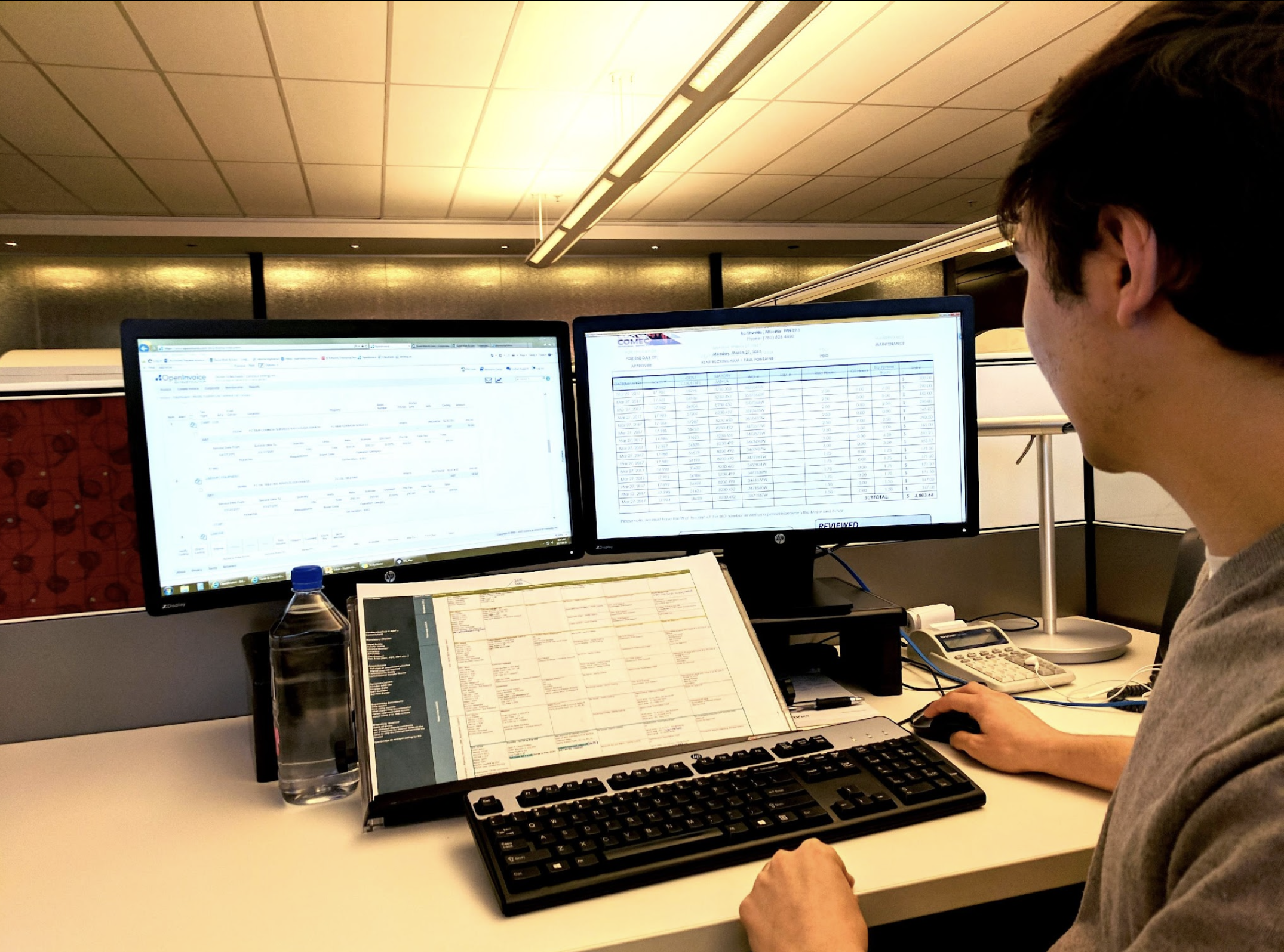 A person works at their desk using OpenInvoice software on a side-by-side monitor setup..