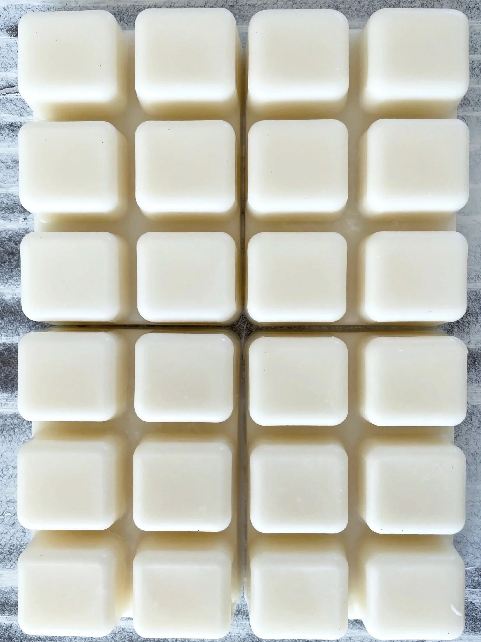 A grid of four rows and four columns of white, rectangular bars of soap or wax, arranged on a light-colored surface.